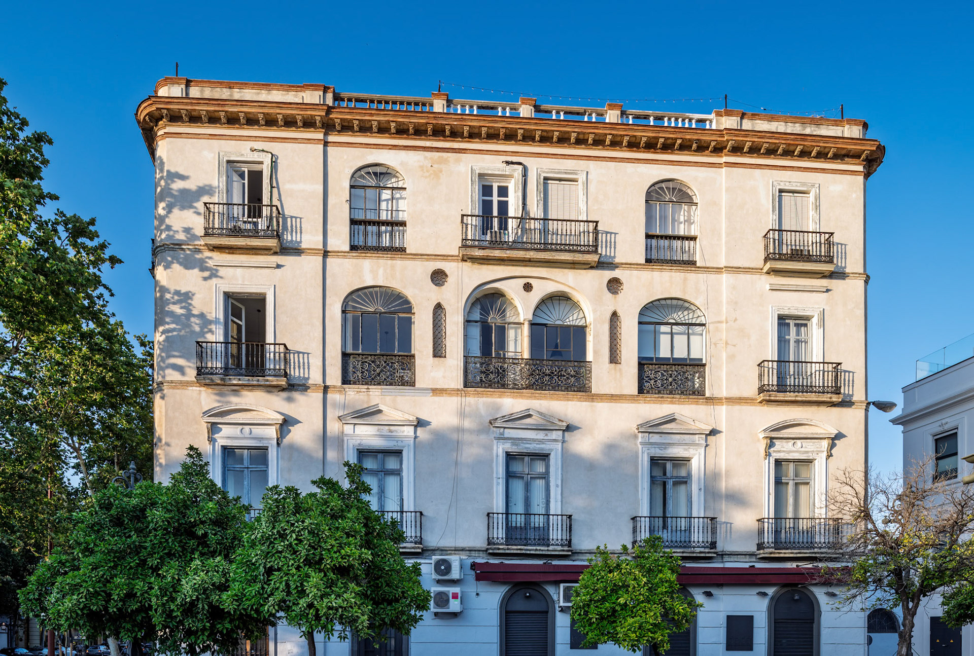 A 19th-century residential building features elegant arched balconies and classical moldings, located at the corner of Paseo de Colón and Reyes Católicos.