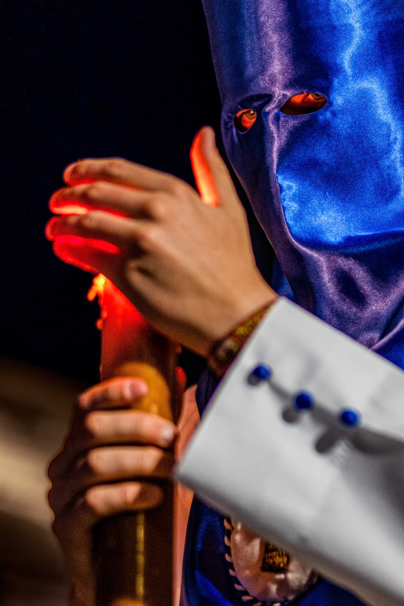 A Hiniesta Brotherhood Nazarene protects his candle's flame with his hand on Palm Sunday night during Holy Week in Seville, Andalusia, Spain.