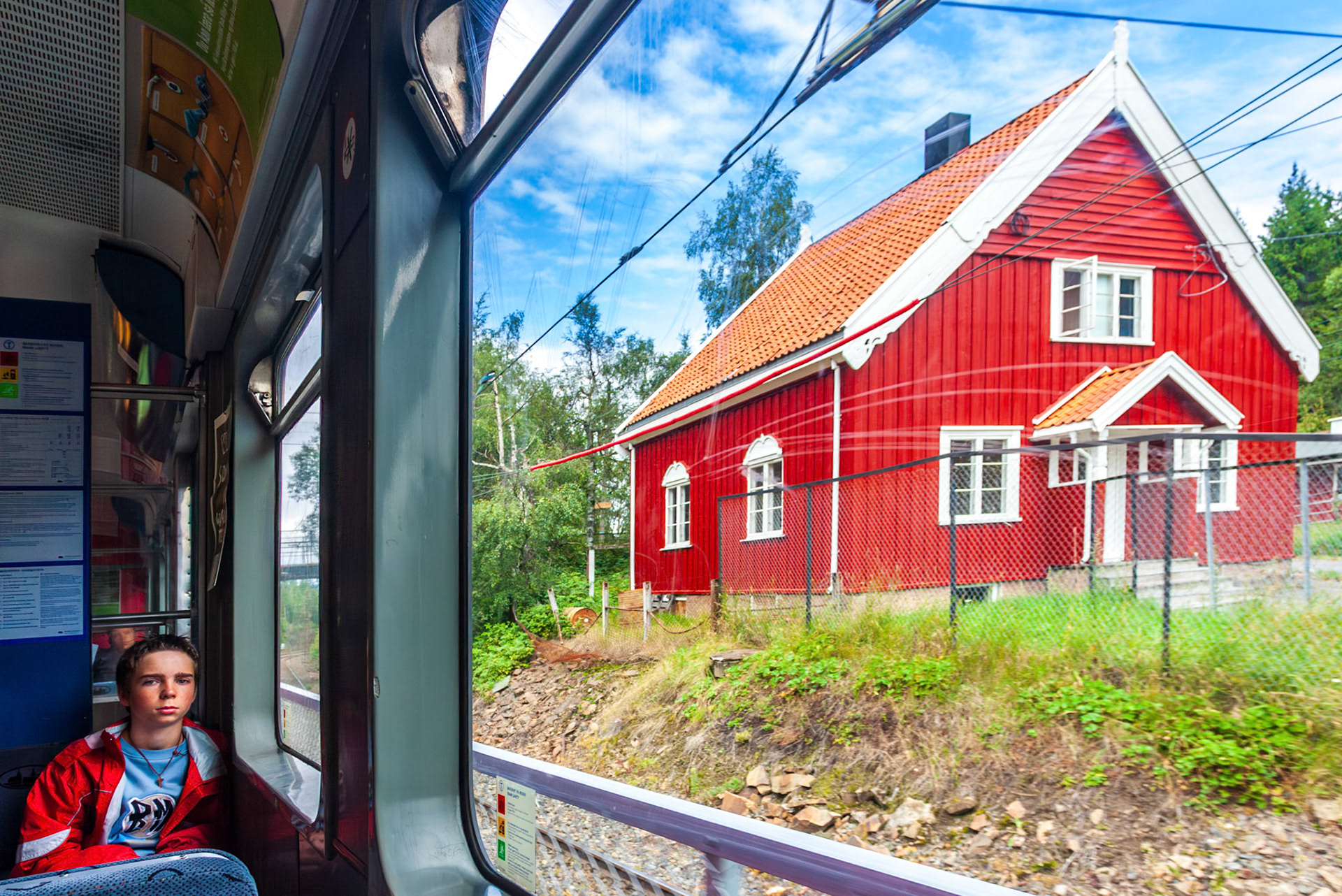 Oslo, Norway, Aug 10 2017, Taking the train through Oslo reveals a vibrant red Scandinavian house surrounded by greenery and a clear blue sky.