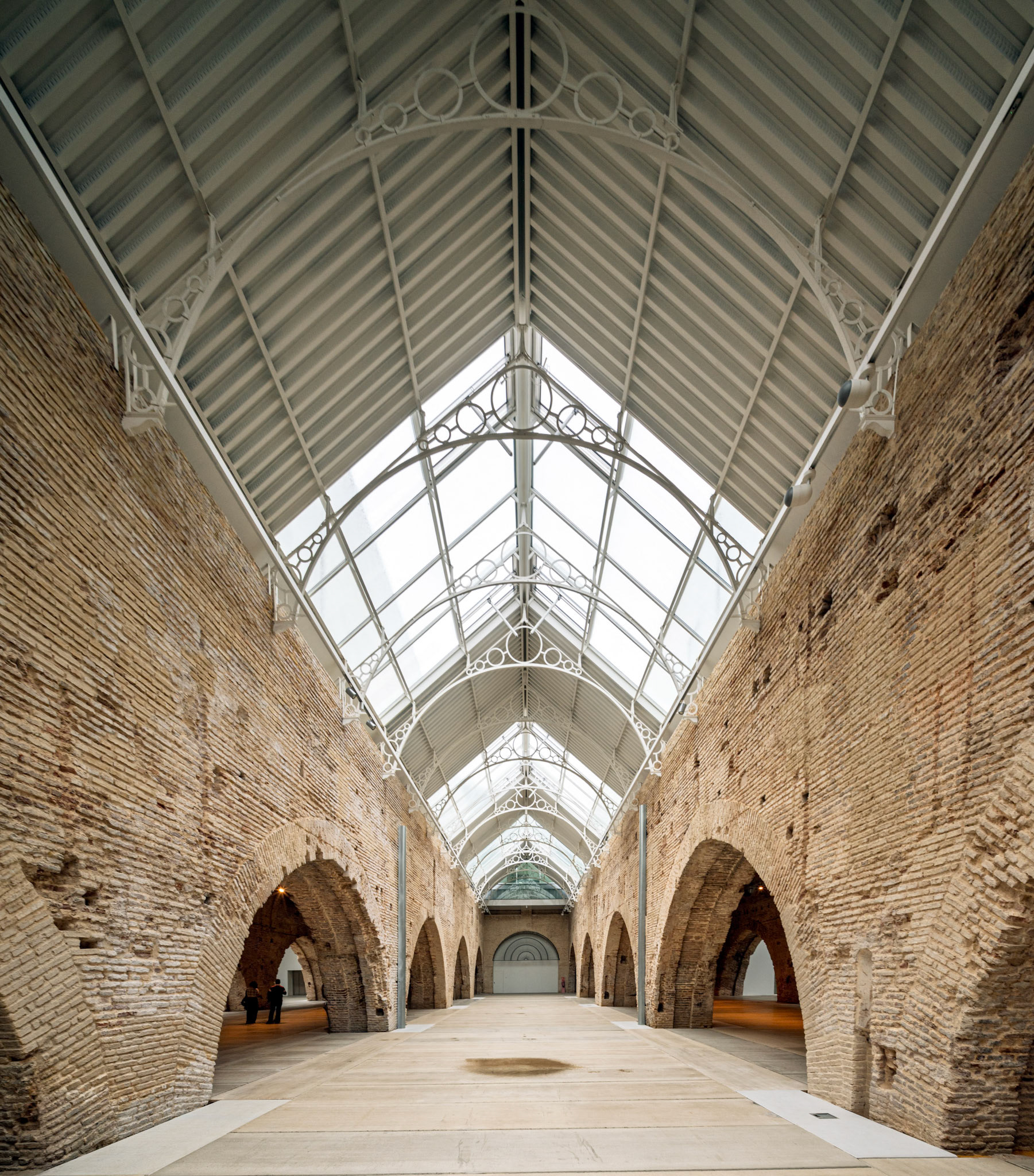 Modern glass roof and iron supports contrast with medieval brickwork in Seville’s Atarazanas, showcasing the city's rich architectural history.