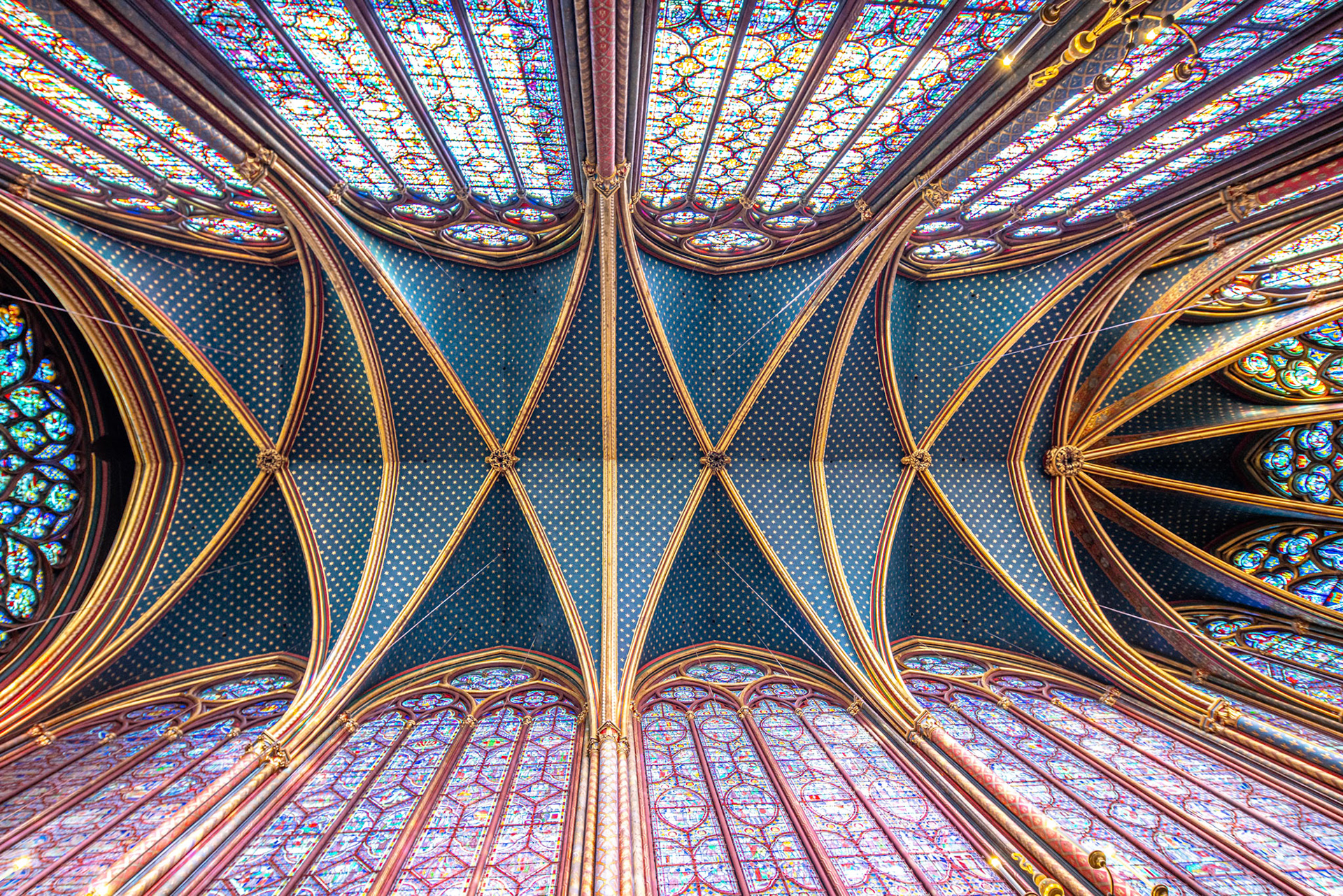 Vaulted ceiling and stained glass windows of Sainte Chapelle, Paris bathed in colorful light.