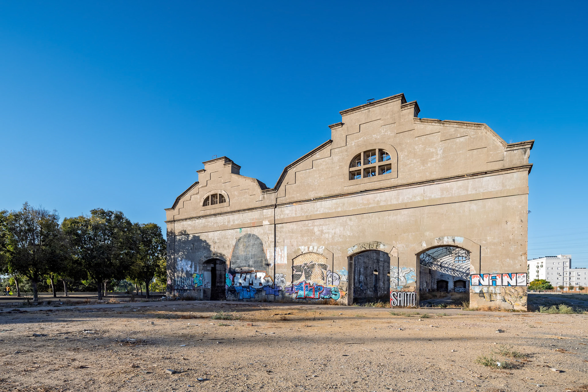 Decades-old Renfe warehouses in Seville are now a tech hub, showcasing urban renewal with graffiti art on brick structures under a clear blue sky.