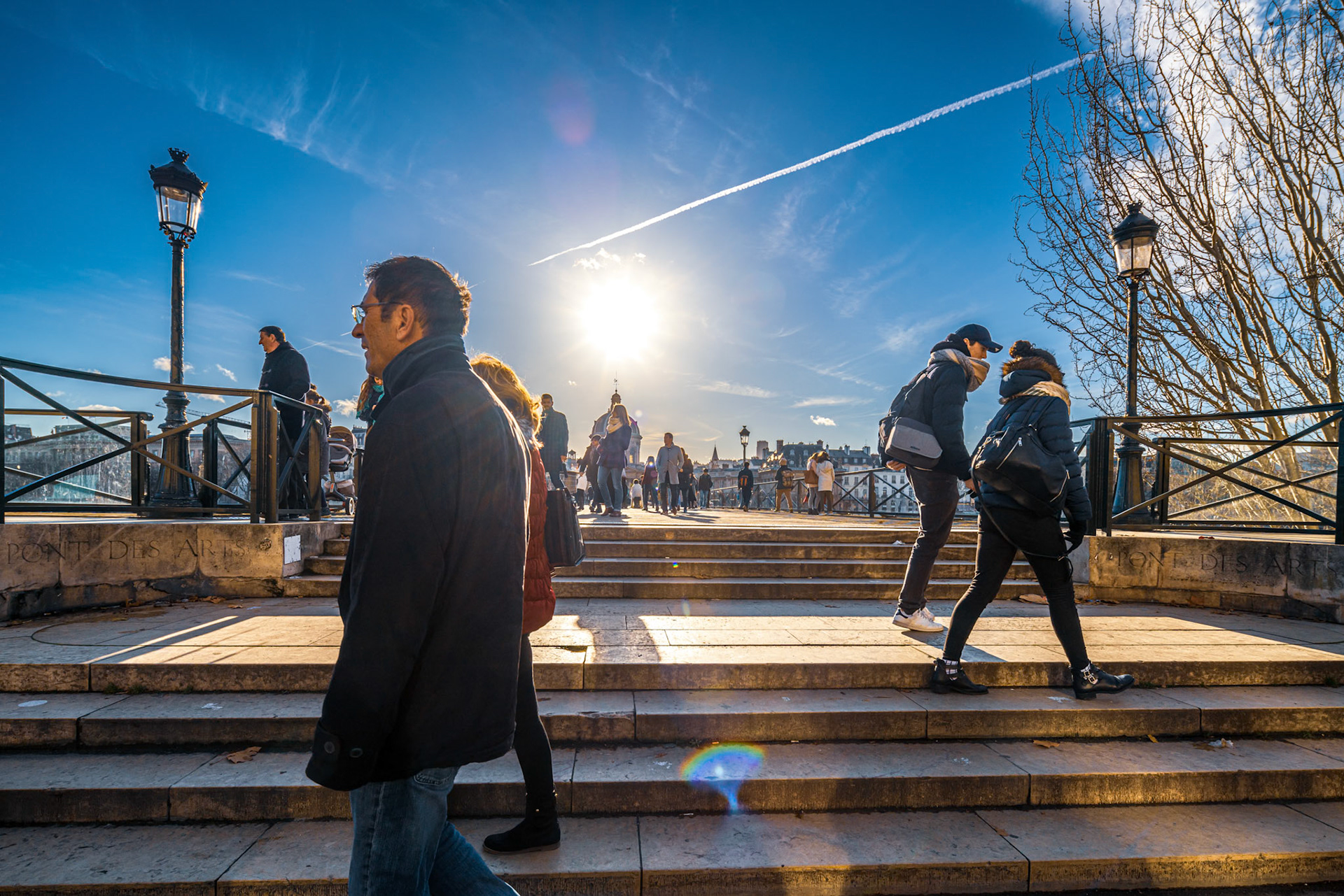 Couples and individuals enjoying the iconic Pont des Arts bridge in Paris under a clear sky.