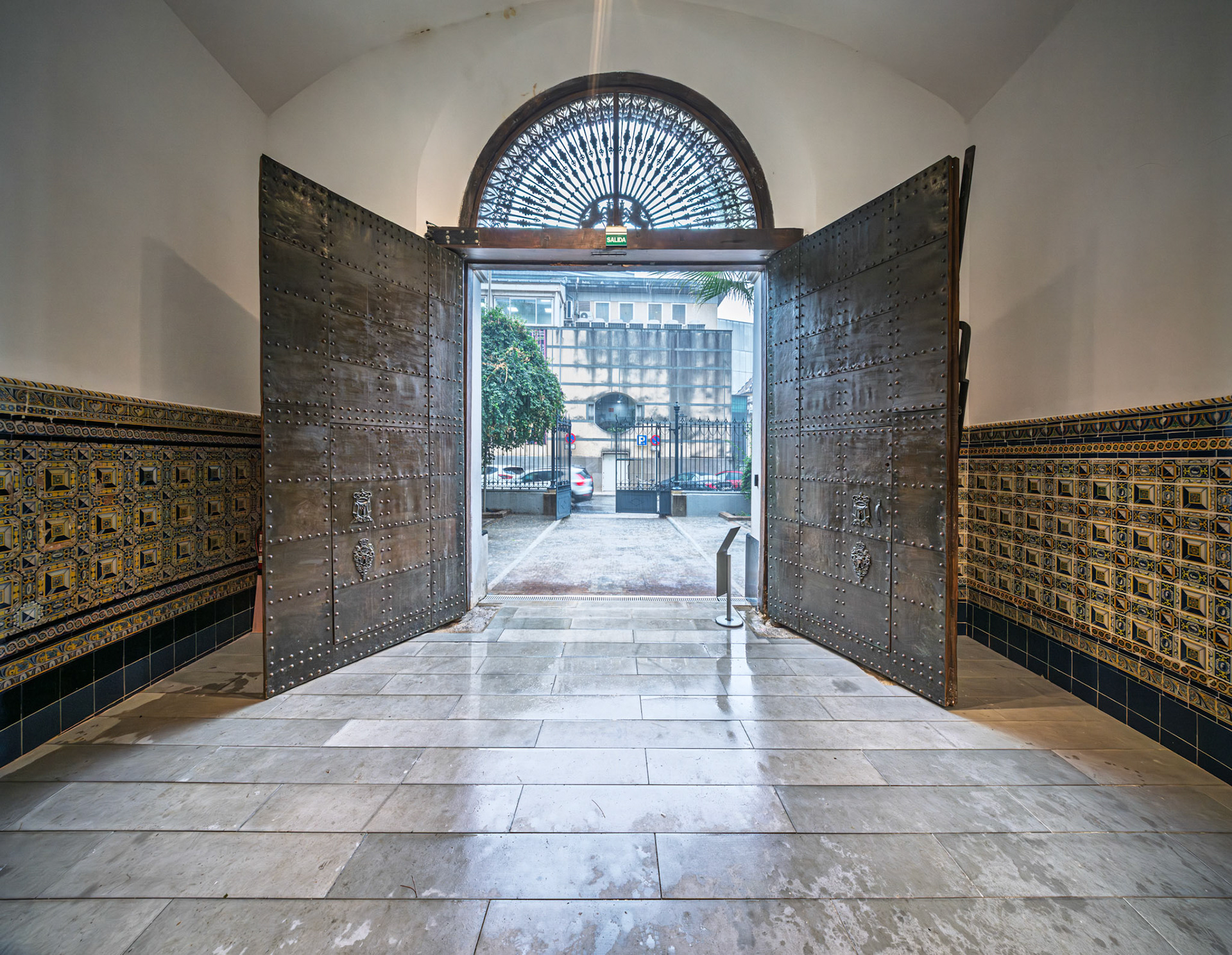 Open iron doors welcome visitors into the Atarazanas in Seville, showcasing beautiful tilework in blue and gold along the walls.
