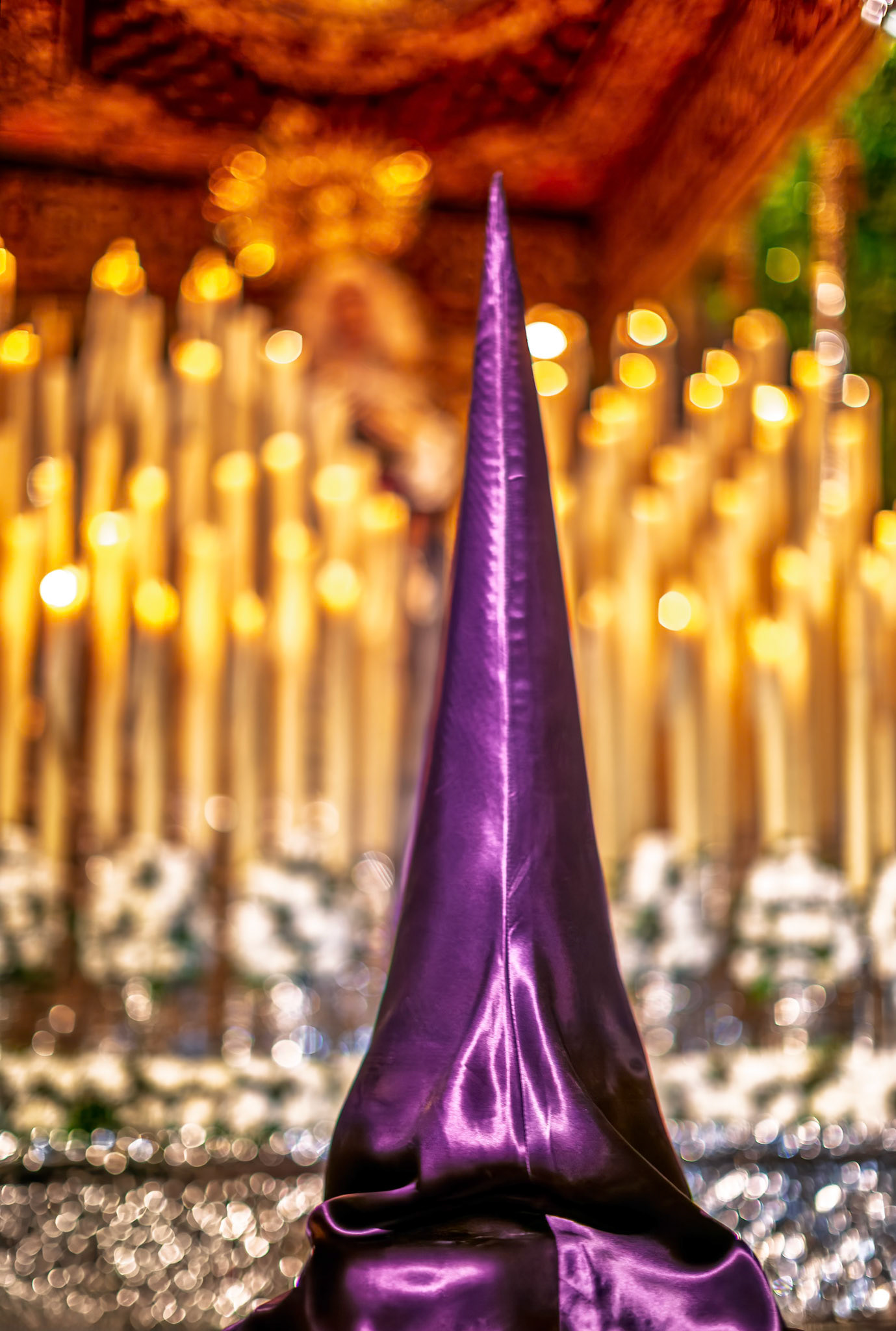 A penitent stands in reverence in front of the Virgin of Victory’s canopy, illuminated by the glow of devotional candles in Seville.
