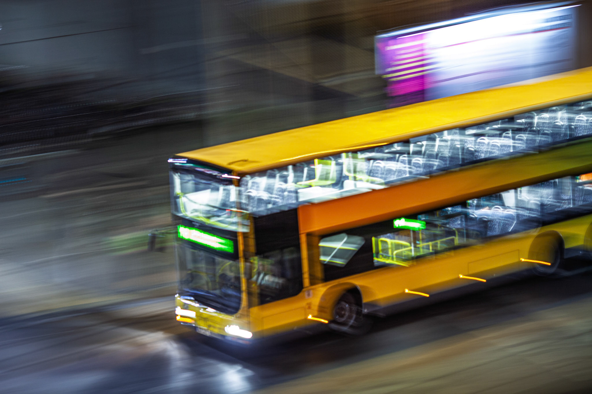 A vibrant yellow bus moves swiftly through the illuminated streets of Berlin at night, showcasing the city's bustling urban life and public transport.