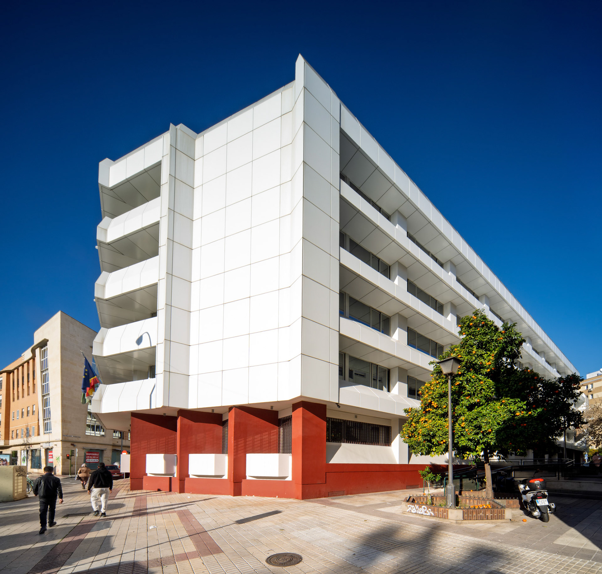 The Instituto Nacional de la Seguridad Social in Seville features a striking white geometric design with a bold red base, set against a clear blue sky.