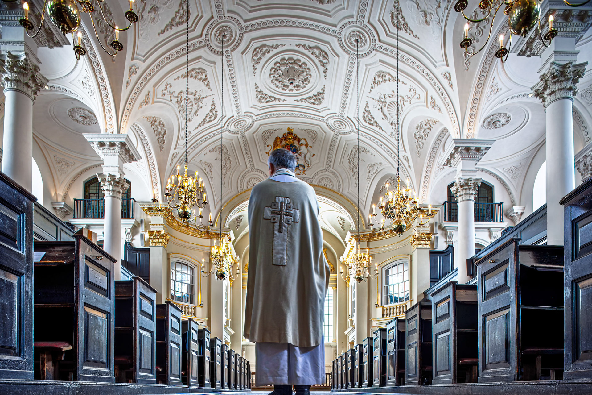 A clergy member stands in the body of Saint Martin in the Fields church during a service. The interior shows ornate ceilings and wooden pews.