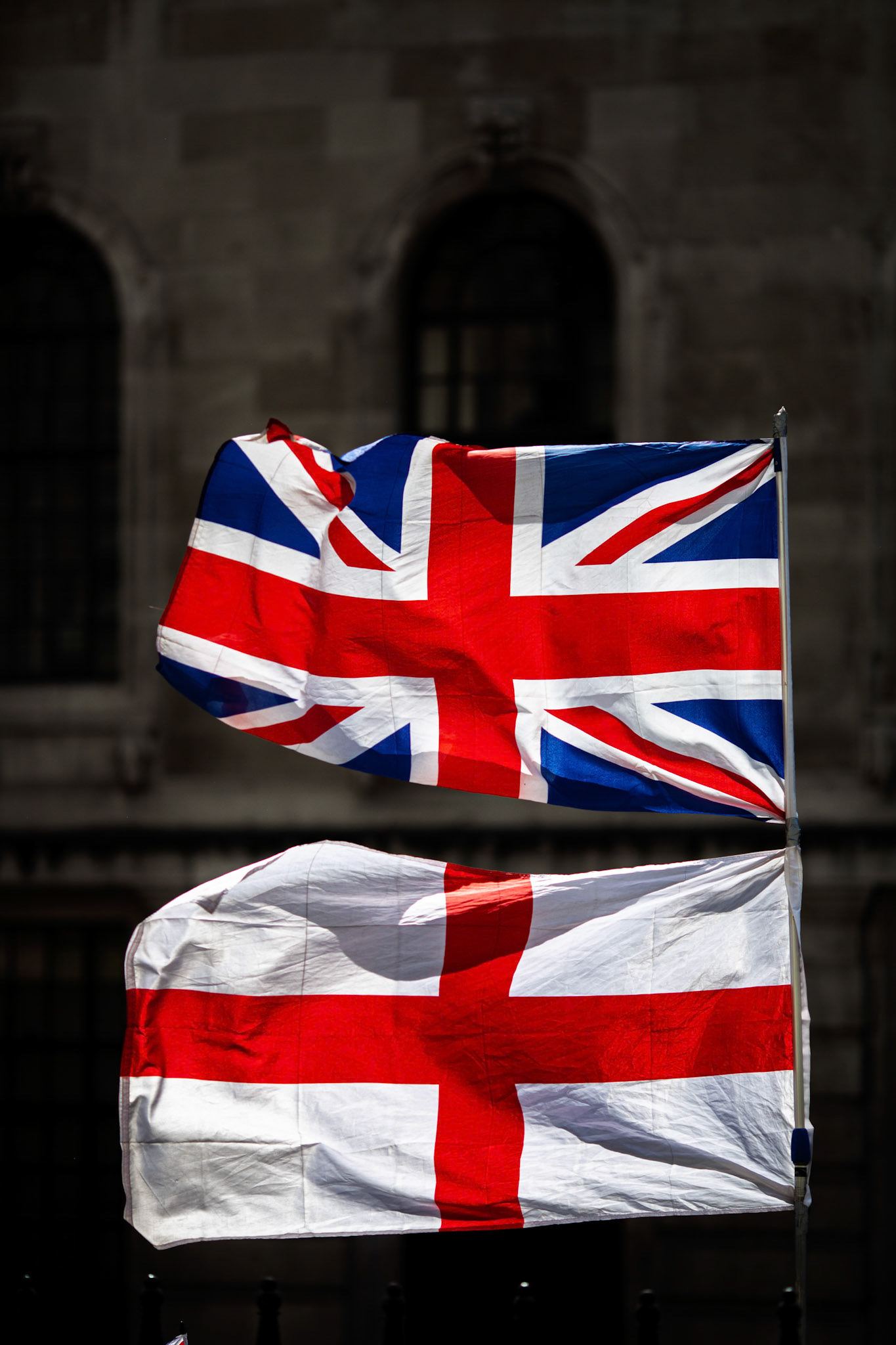 Union Jack and Saint George's Cross flags displayed outdoors against a historic building.