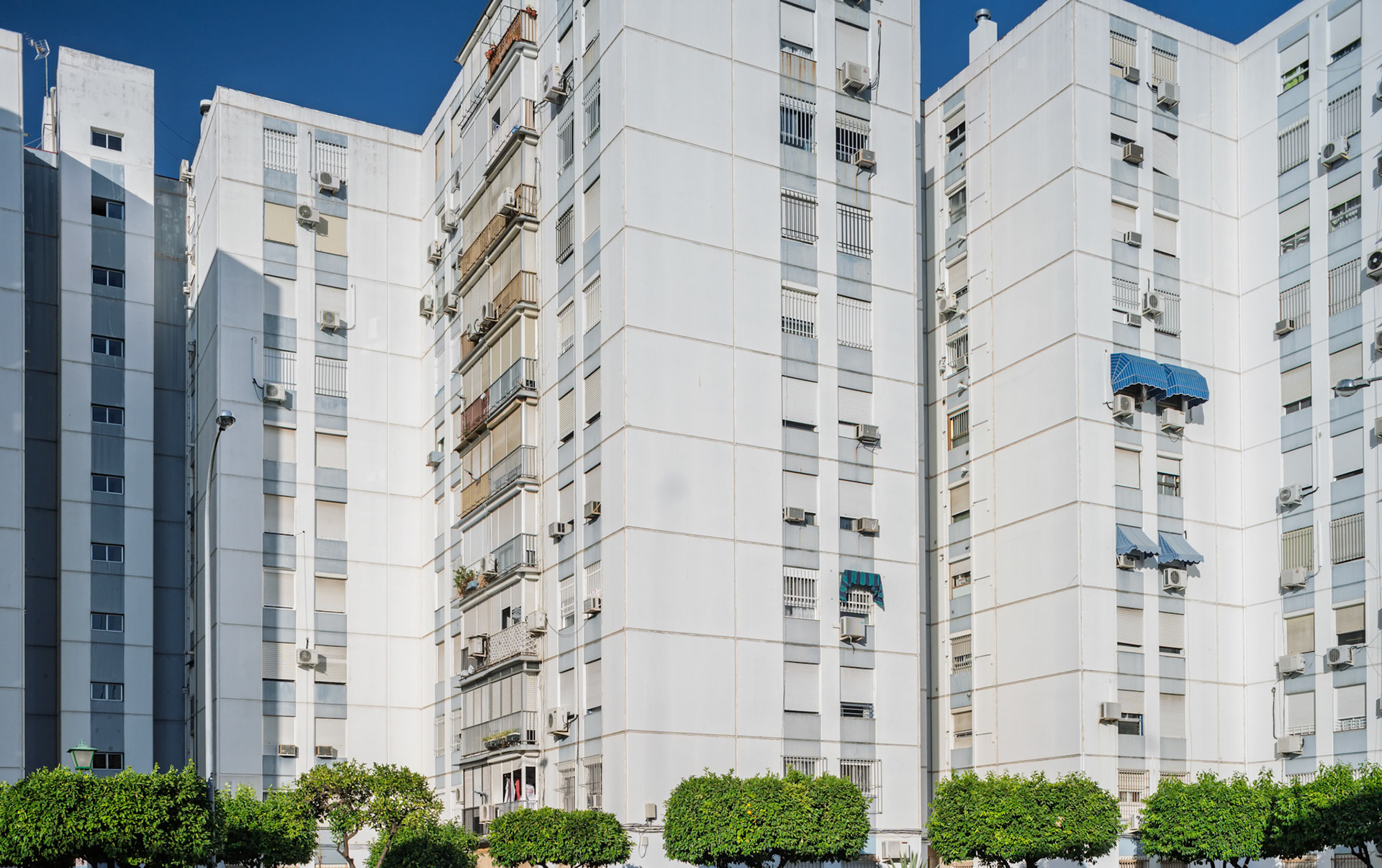 White façades of residential buildings in northern Seville illustrate late 20th-century urban growth, featuring balconies and air conditioning units.