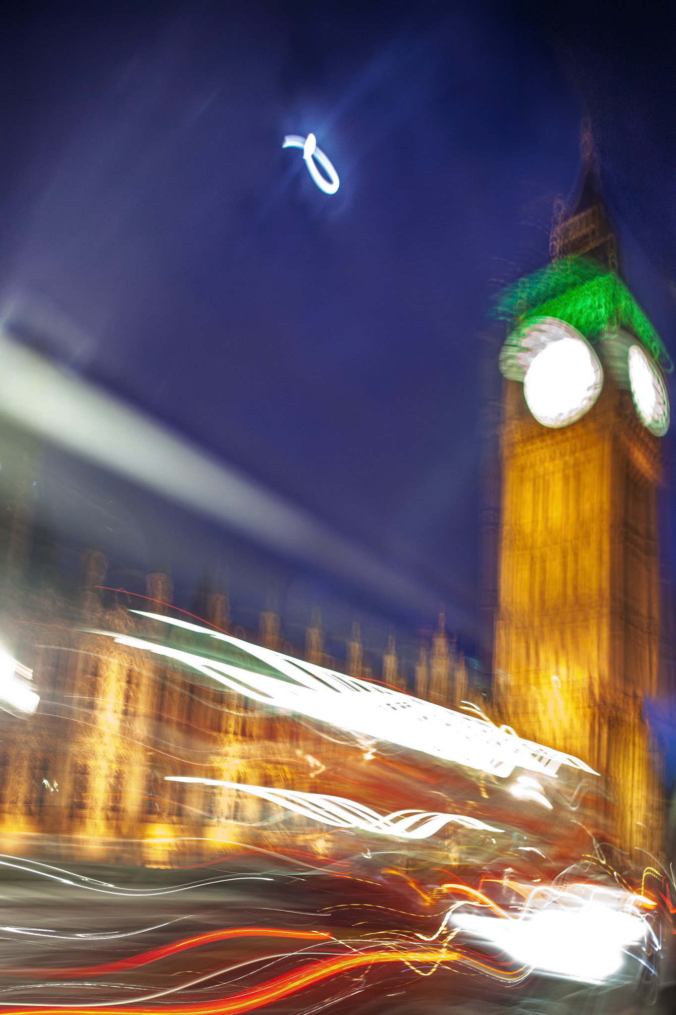Big Ben stands tall in London while colorful lights streak by from a moving vehicle at night, showcasing the city's vibrant energy and motion.