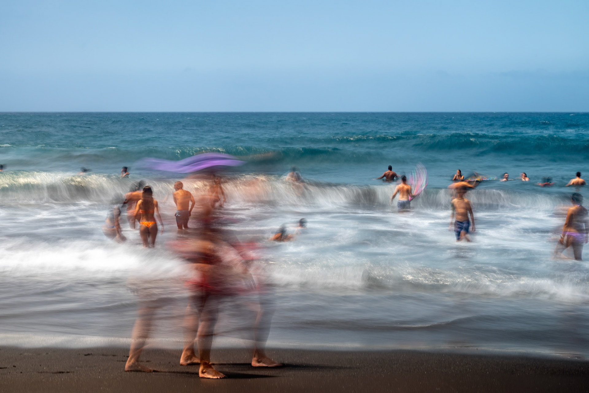 Long exposure of people enjoying the waves at Bollullo Beach in La Orotava, Tenerife, in the Canary Islands.