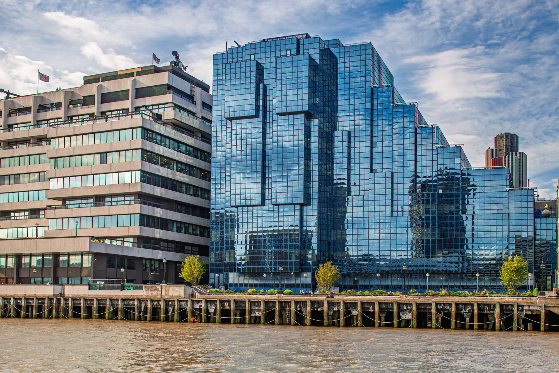 The Northern and Shell Building stands by the Thames river near London Bridge. Its glass facade reflects surrounding structures under a clear sky.