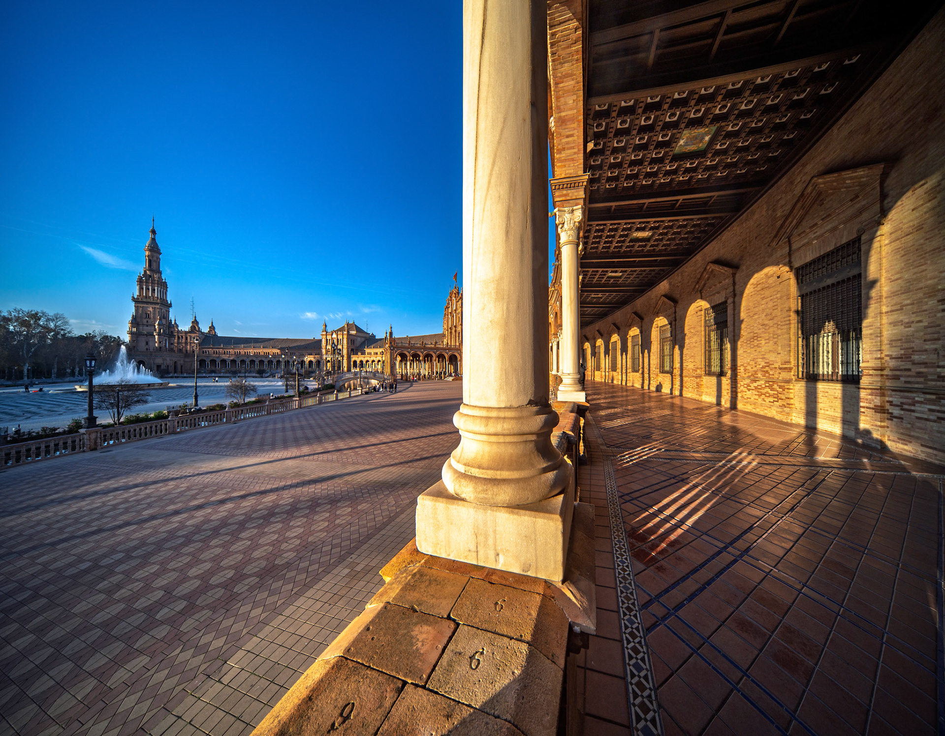 Low-angle view of Plaza de Espana reveals stunning columns and arches under warm light, highlighting intricate tiles and the vibrant atmosphere of Seville.