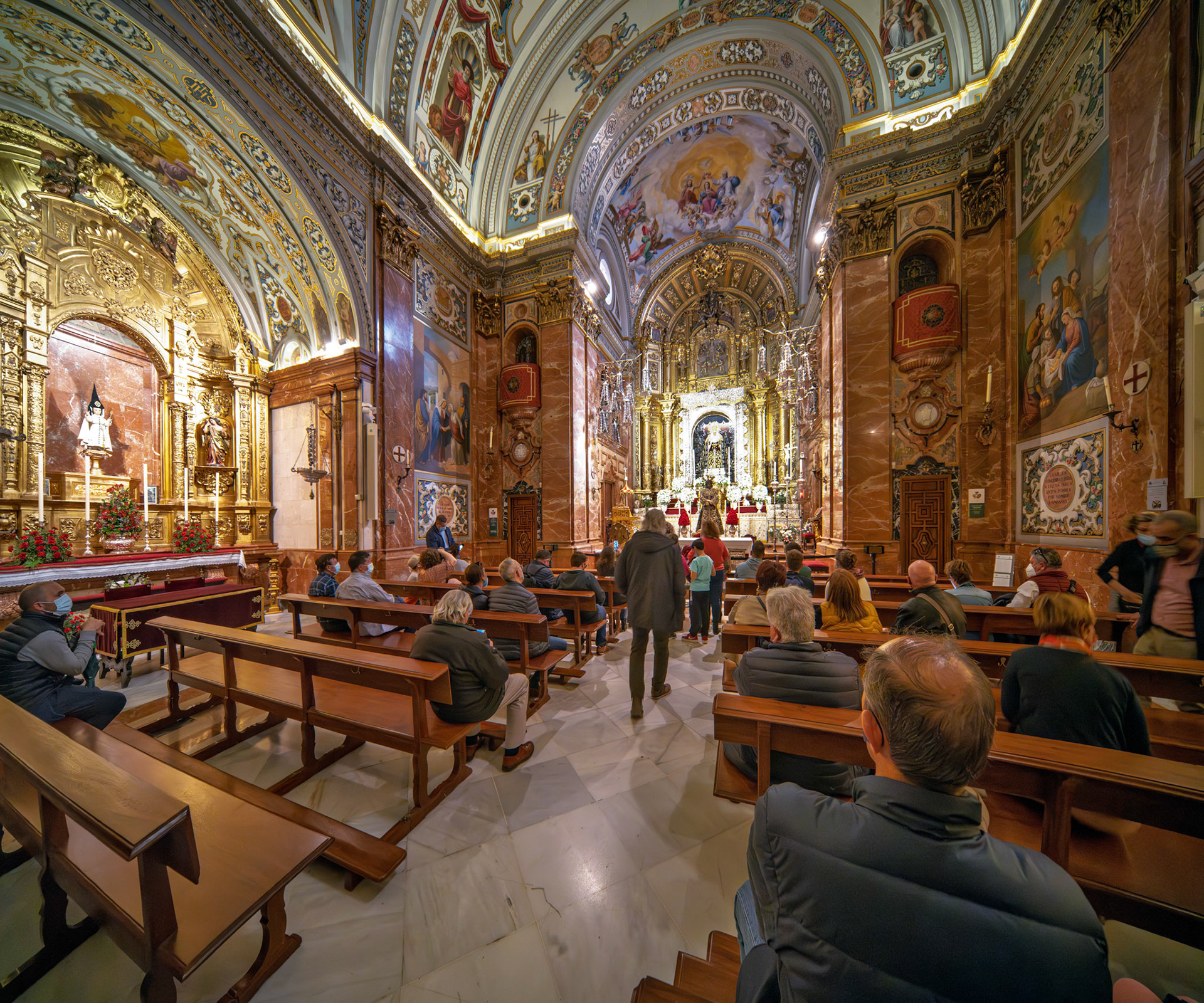 Worshippers crowd the pews of Basílica de la Macarena in Seville, amidst glowing vaults and exquisite religious art, showcasing their devotion.