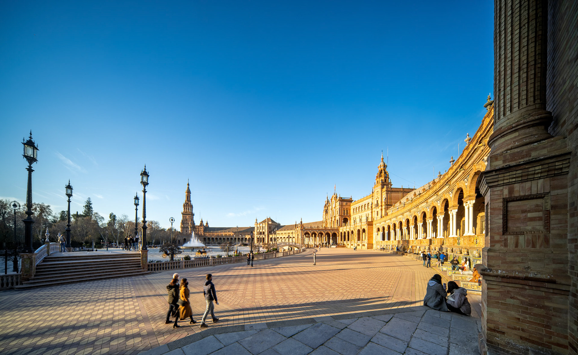 Soft winter light bathes Plaza de España, highlighting warm tones and gentle shadows as visitors stroll leisurely through the expansive space.