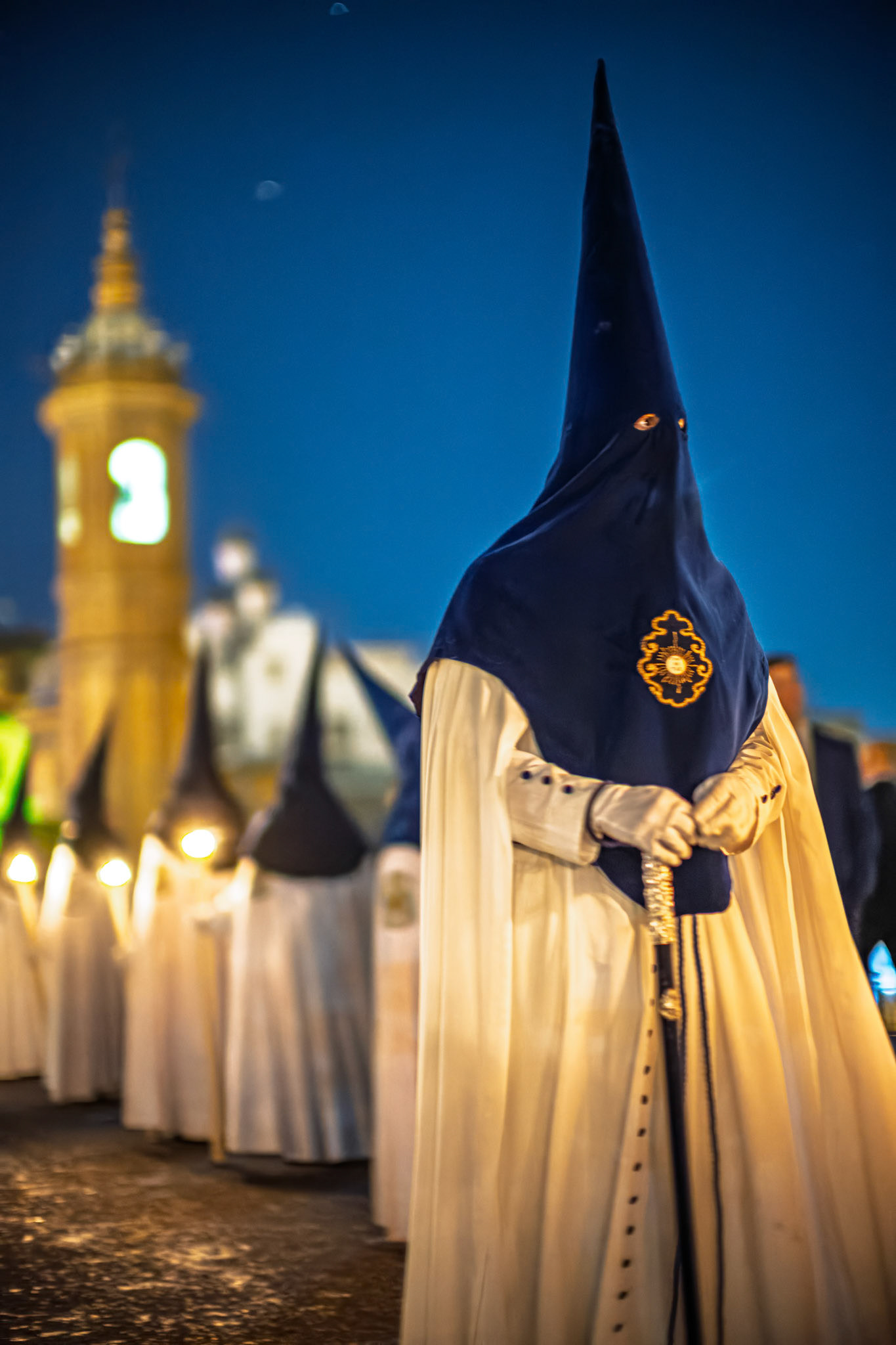 A Nazarene from La Estrella Brotherhood, a section deputy, observes the Holy Week procession on Palm Sunday night near Triana Bridge's Carmen Chapel, Seville.