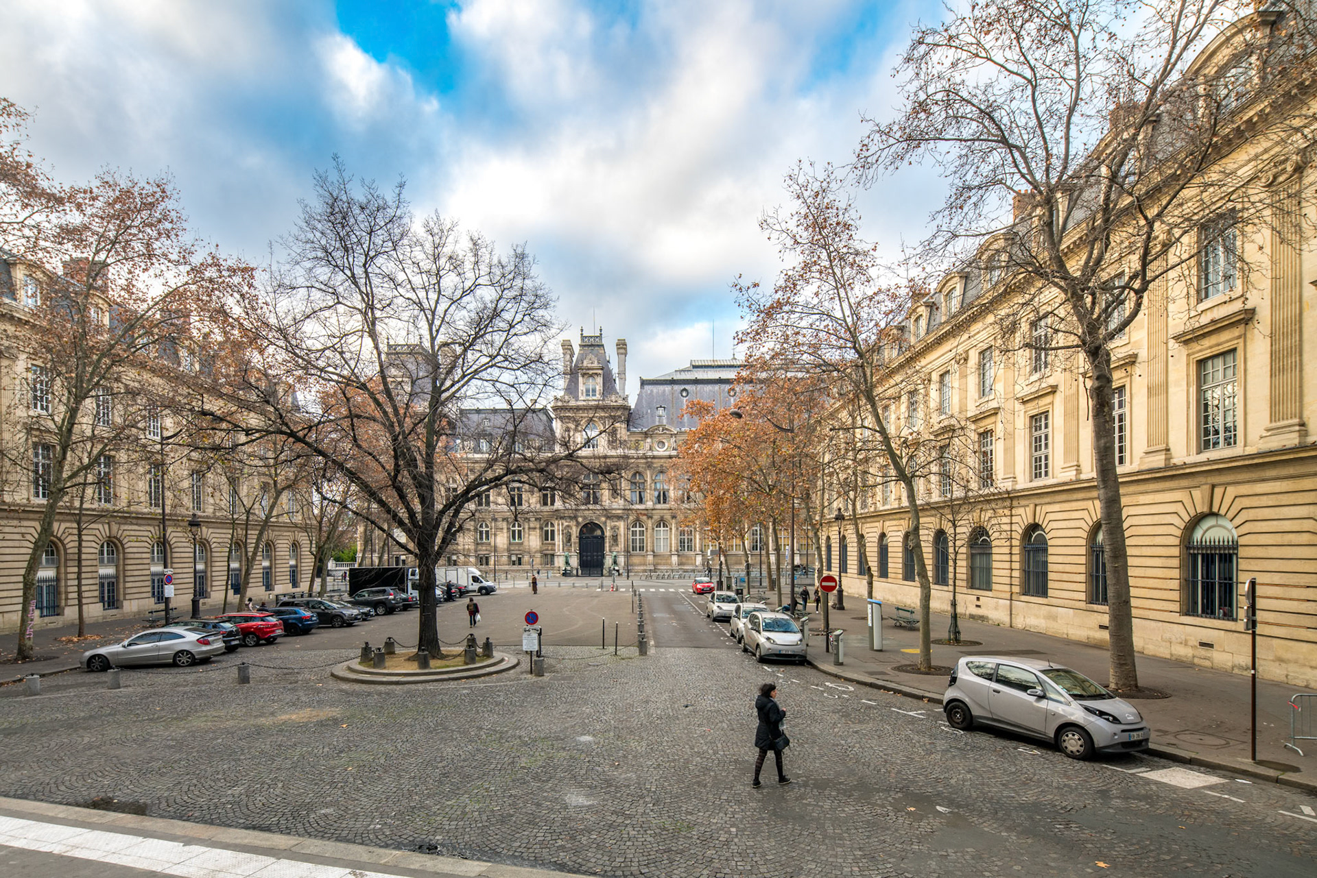 A person walks through a tree-lined Saint-Gervais-Saint-Protais square with the Hôtel de Ville in Paris in the backdrop.