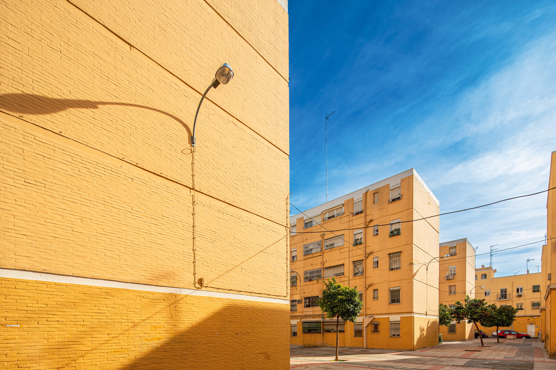 Brick buildings with barred windows and tiled sidewalks showcase Seville's dedication to affordable living and urban dignity in La Barzola.