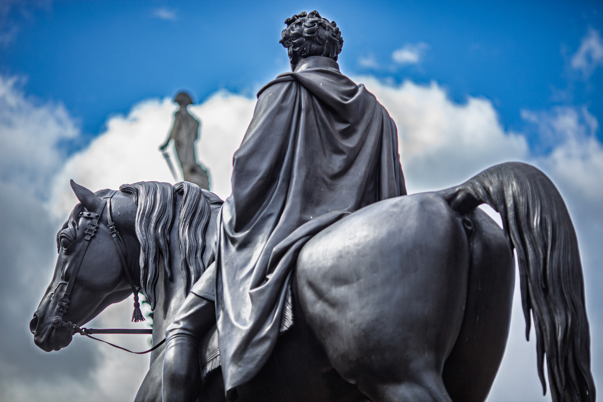George IV statue stands on a horse, looking towards Nelson's column in Trafalgar Square, London. Clouds fill the sky in the background.