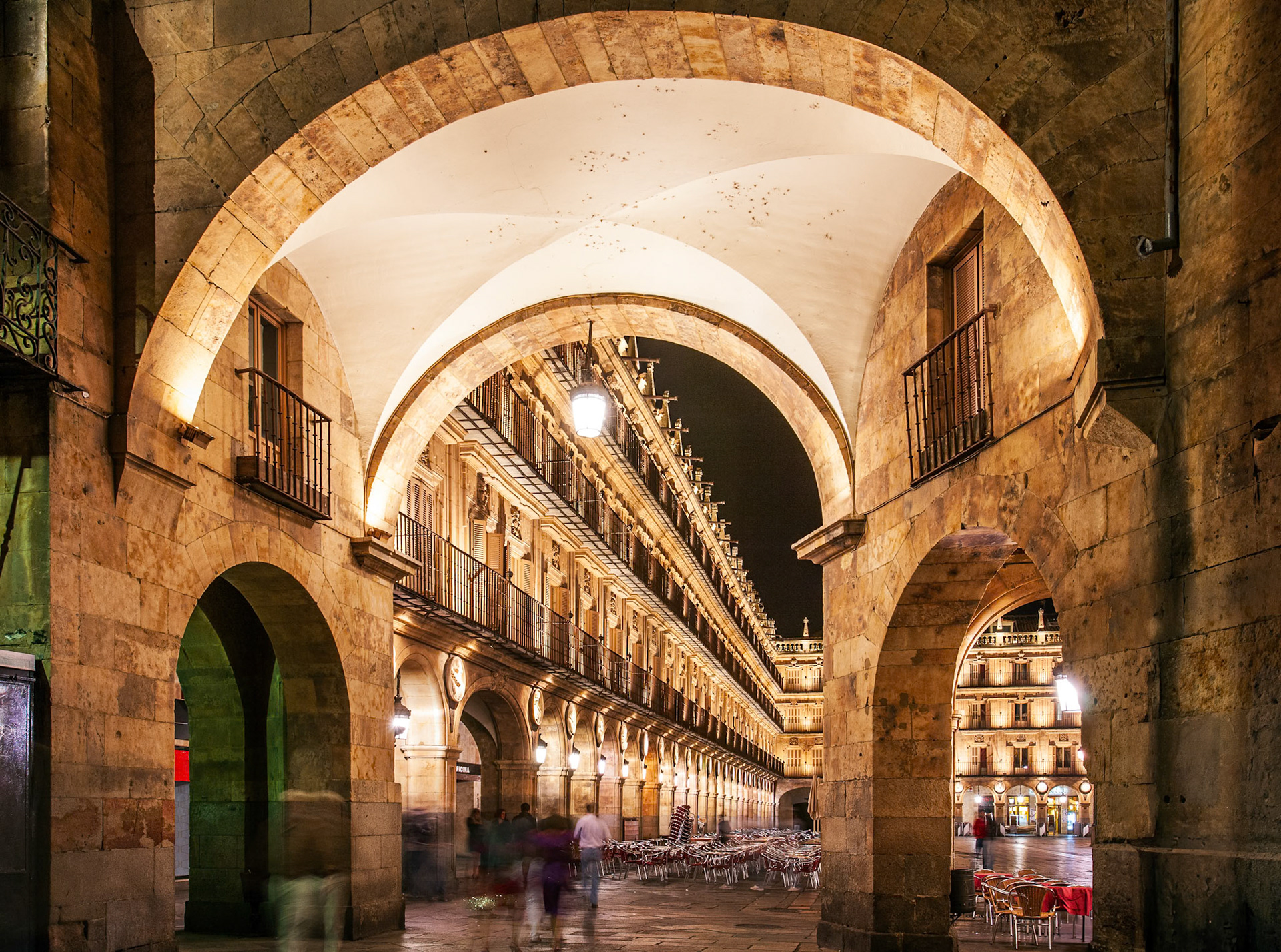A nighttime view of Plaza Mayor in Salamanca seen through illuminated stone arches.