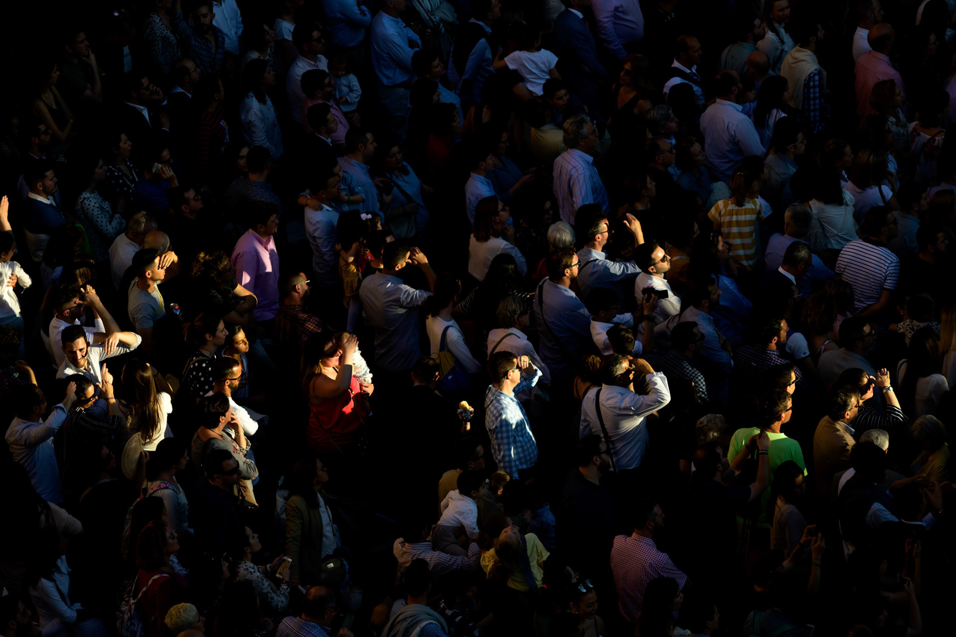 An eager crowd in Seville, Andalusia, Spain, watches a Holy Week procession illuminated by the warm afternoon sun. People gather for the religious celebration.