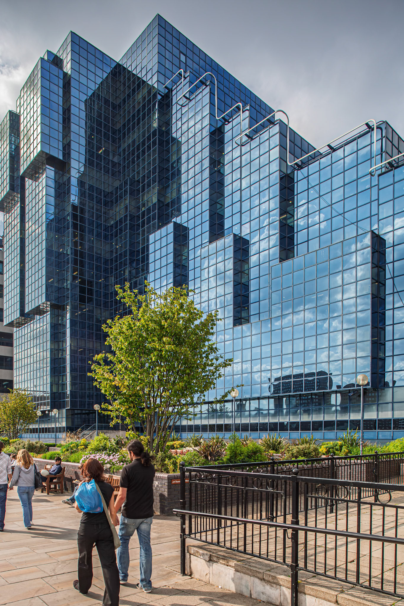 People walk past the Northern and Shell Building near London Bridge. The glass tower reflects the sky and surroundings in the city of London.