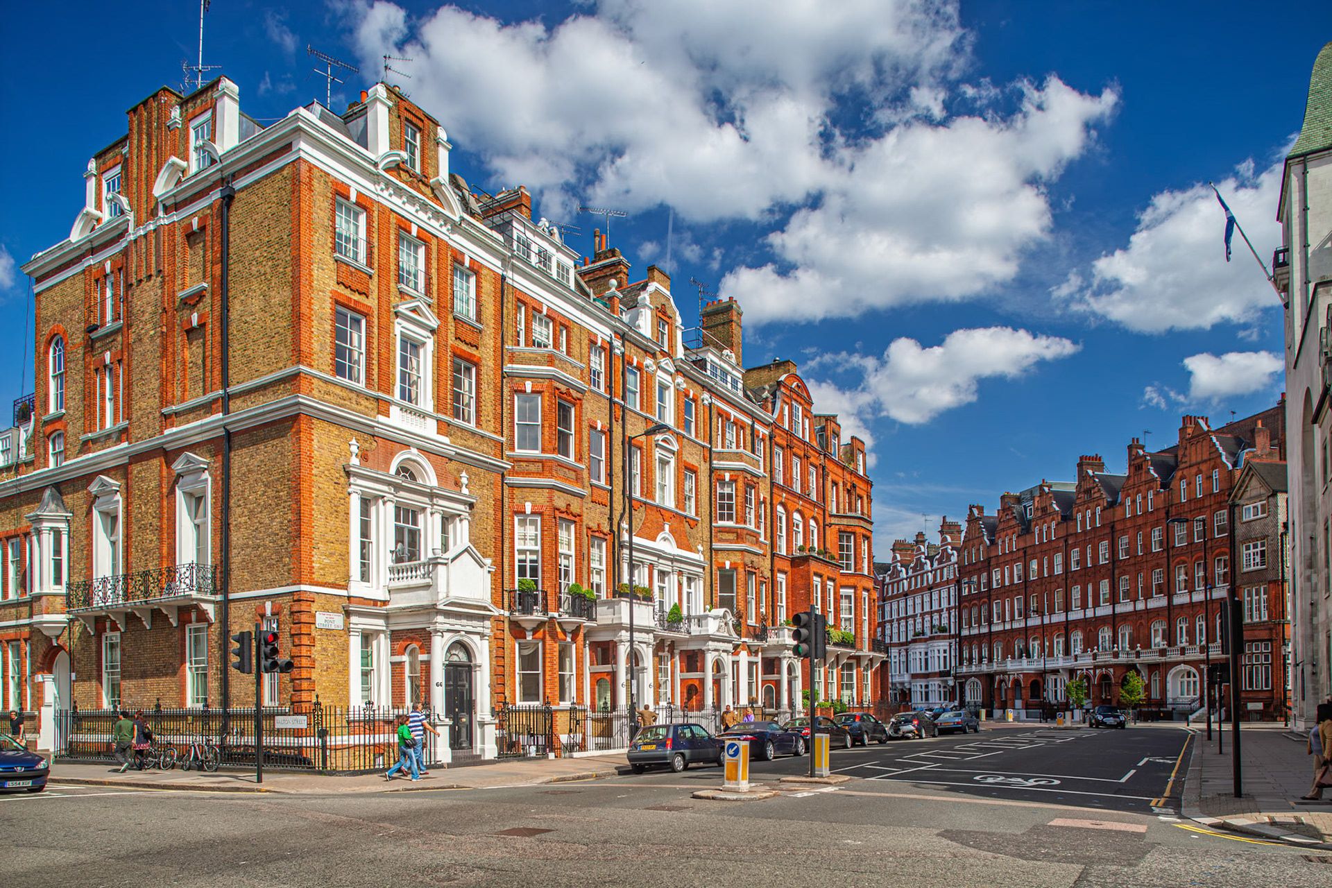 Red brick Victorian houses line Pont Street in Kensington, London, under a blue sky with clouds, showcasing classic urban design and structure.