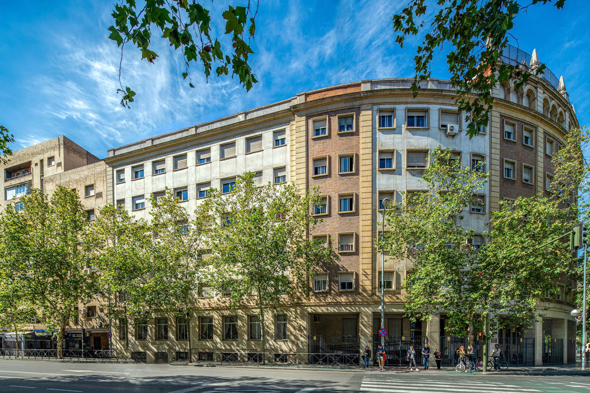 Residential building basked in sunlight at Prado de San Sebastian, with pedestrians and greenery.