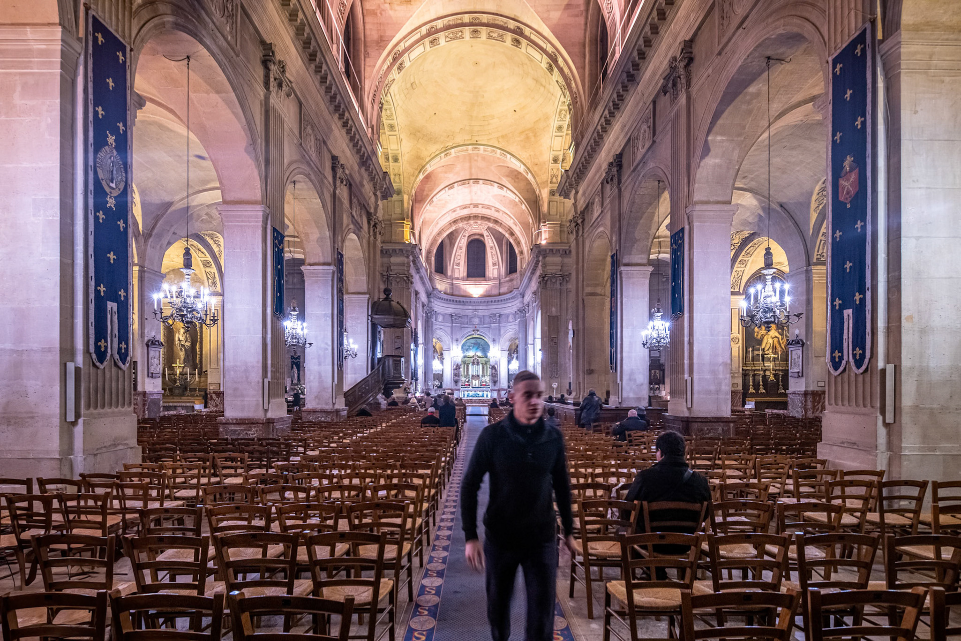 Visitors quietly exploring the grand aisle of Saint-Nicolas-du-Chardonnet church.
