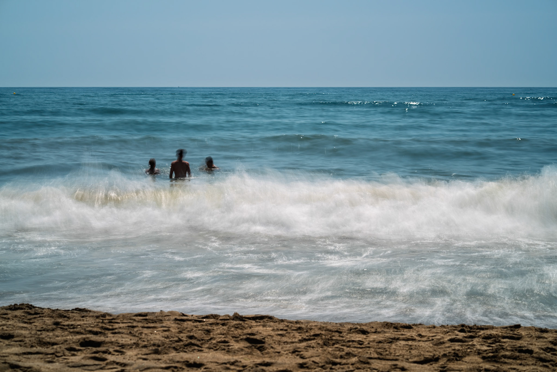 Families and friends play and swim in the warm waters of Isla Canela beach under bright daytime light in Andalusia, Spain.