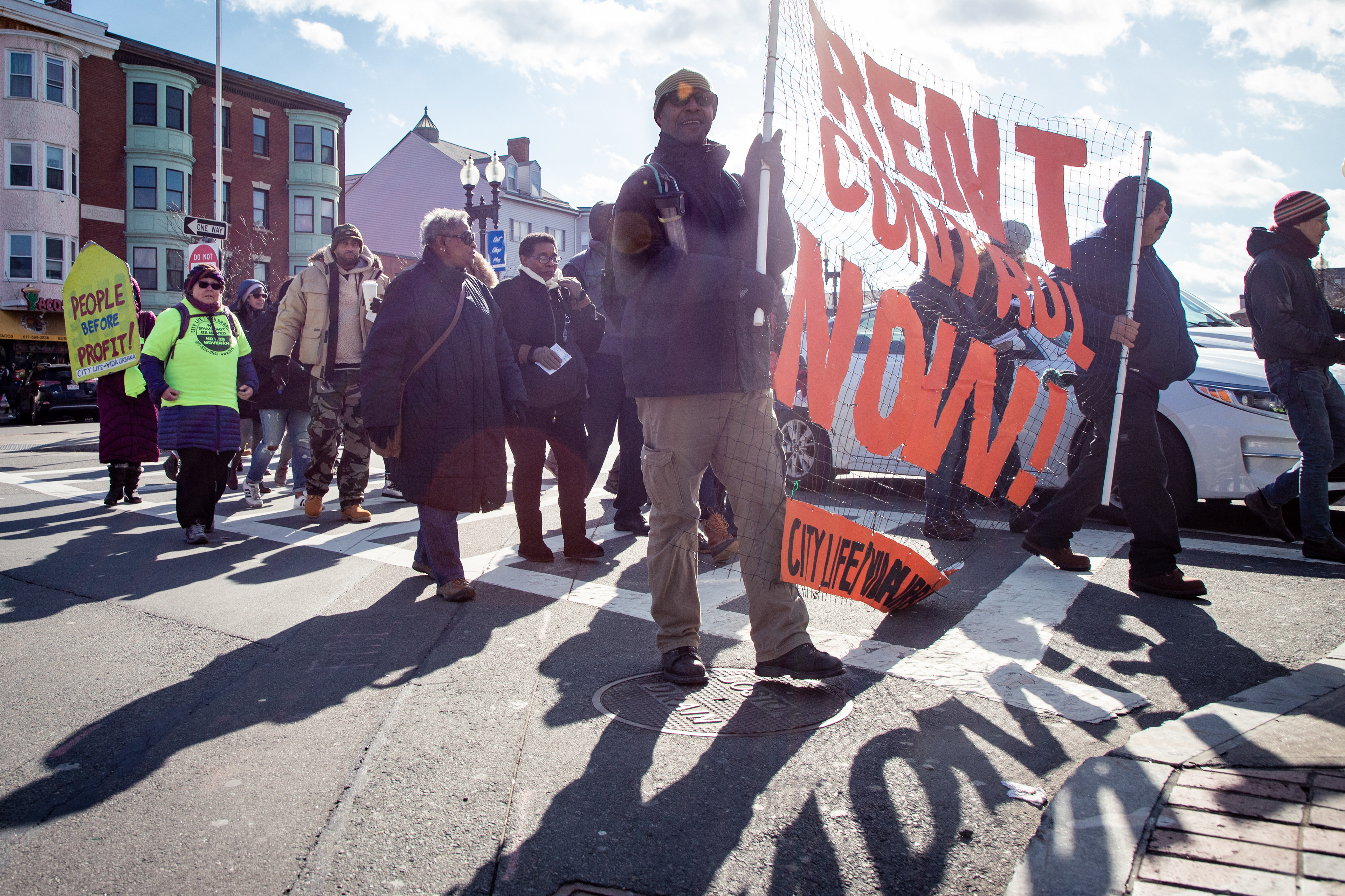 Philip Myrick (center) marches with a banner that reads, “Rent control now!” in an affordable housing protest February 8, 2020 in East Boston. East Boston is home to the highest percentage of immigrants out of all of the city's neighborhoods, and residents are organizing to prevent luxury condo development on a former Amazon bid site from pushing them out.