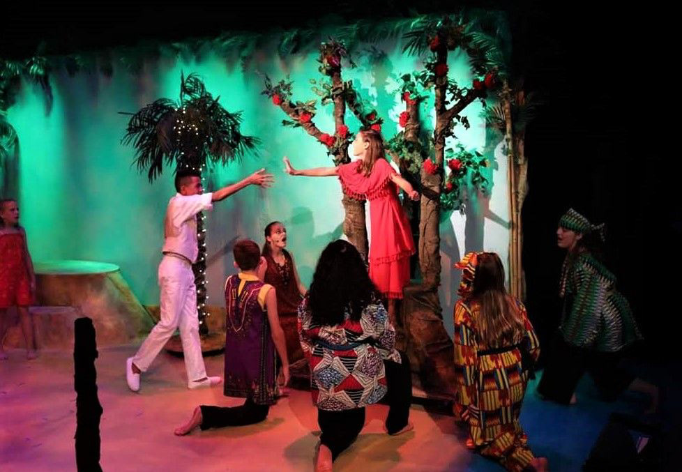 TI MOUNE IN TREE REACHING OUT TO DANIEL WHILE STORYTELLERS SURROUND HER