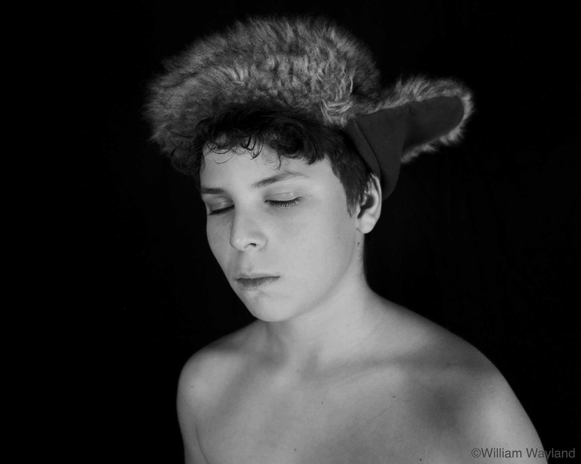Black and white portrait of a boy with no shirt wearing a furry hat