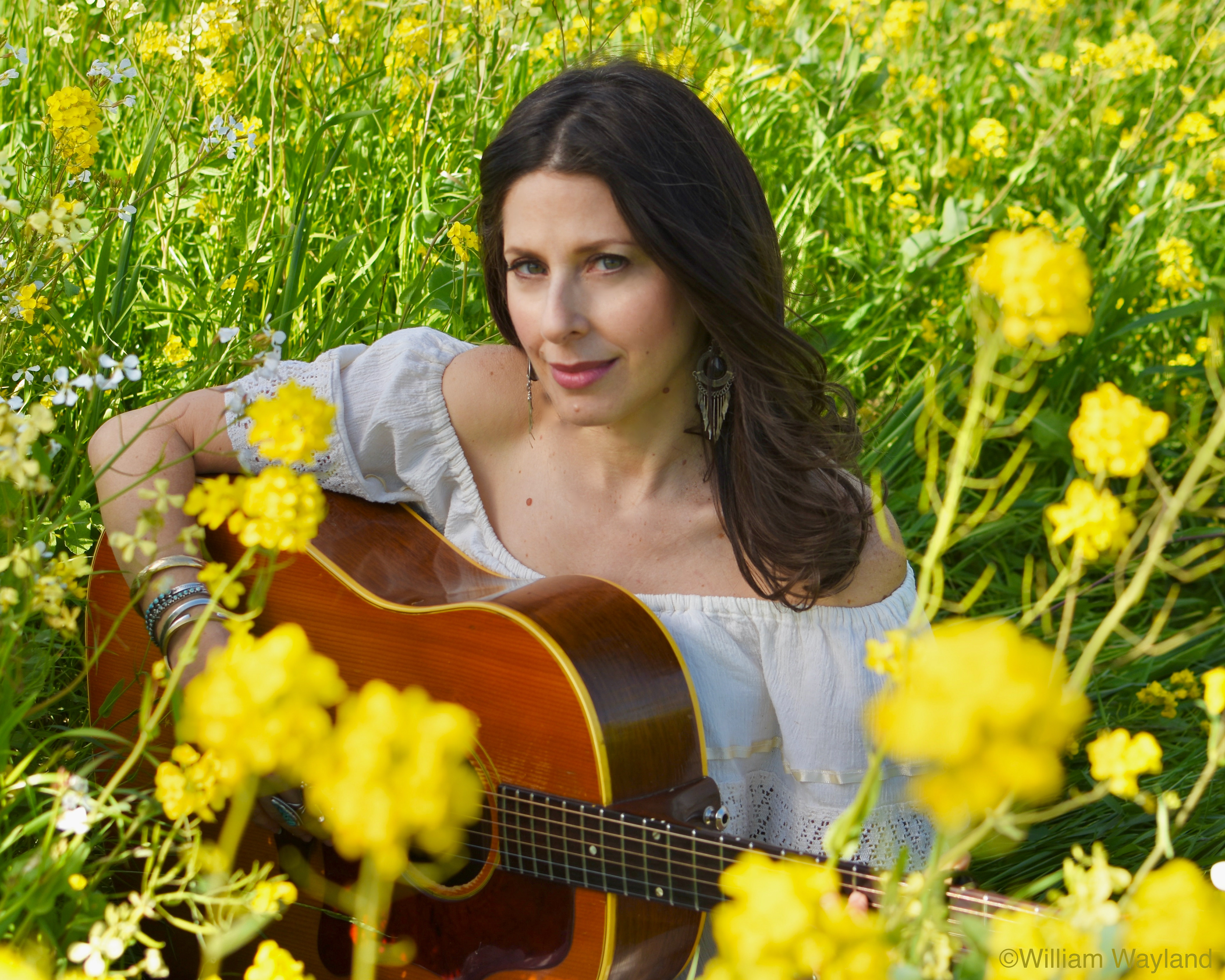 Photograph of country music musician Essence Goldman playing guitar in a field of yellow flowers