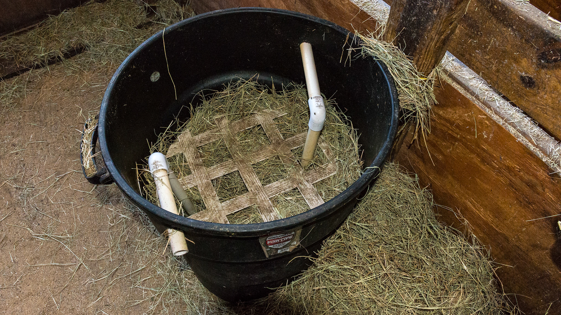 Self made slow hay feeder using a garbage pail, pipe and lattice