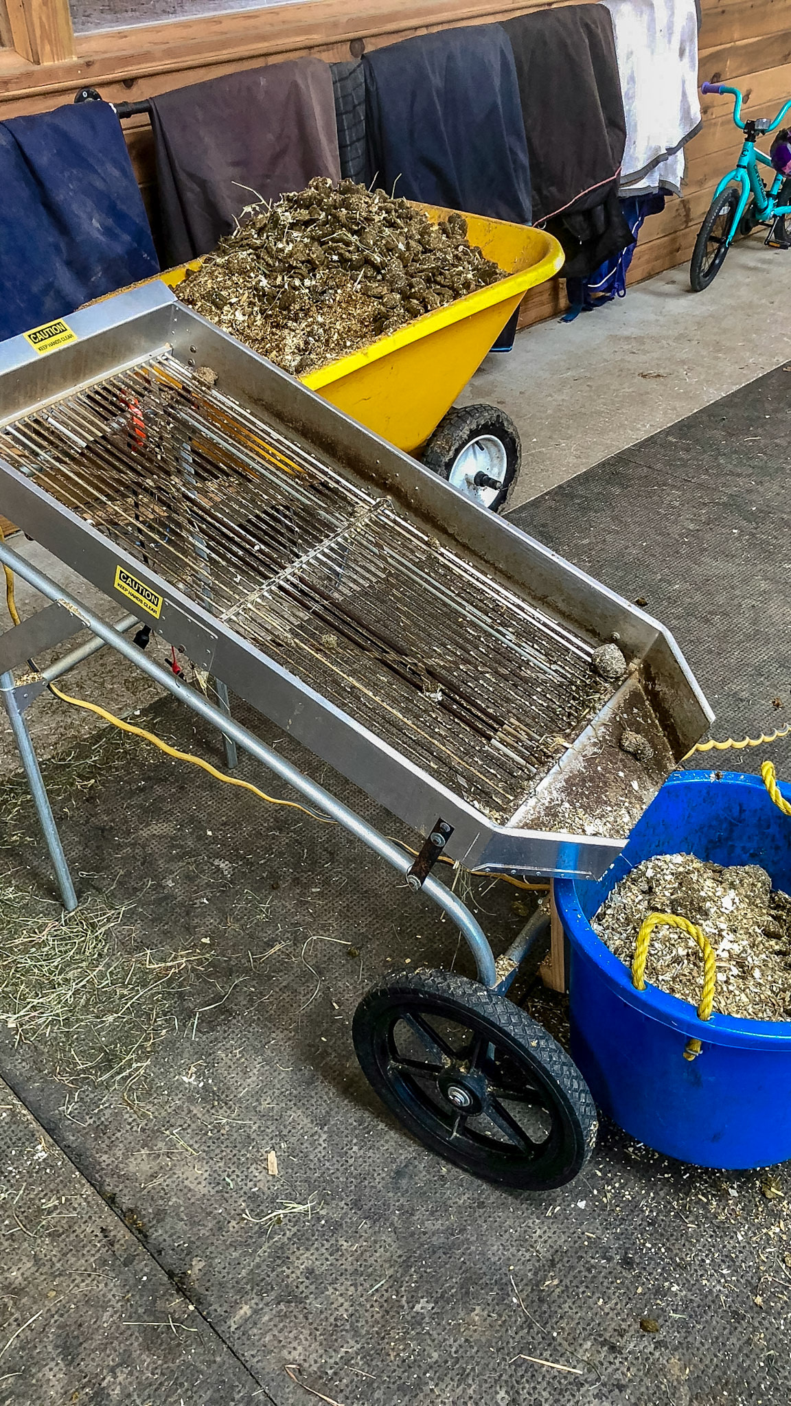 The Shaker is a noisy device run by a high speed drill that sifts the dirty shavings allowing the small dry flakes to fall back into the stall while the larger manure balls roll into the wheel barrow.  With a bit of time, the wet flakes become dry.
