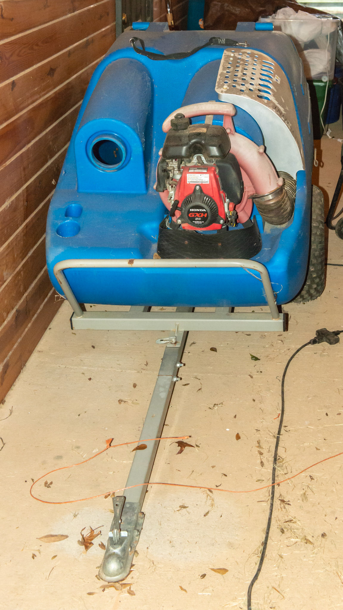 The Greyston manure vaccuum is pulled with a small riding tractor. A large diameter hose is attached to the hole next to the engine. While driving through the paddock, the end of the hose is directed over a manure pile and sucked into the blue container.  Manure can then be composted and used on the garden.