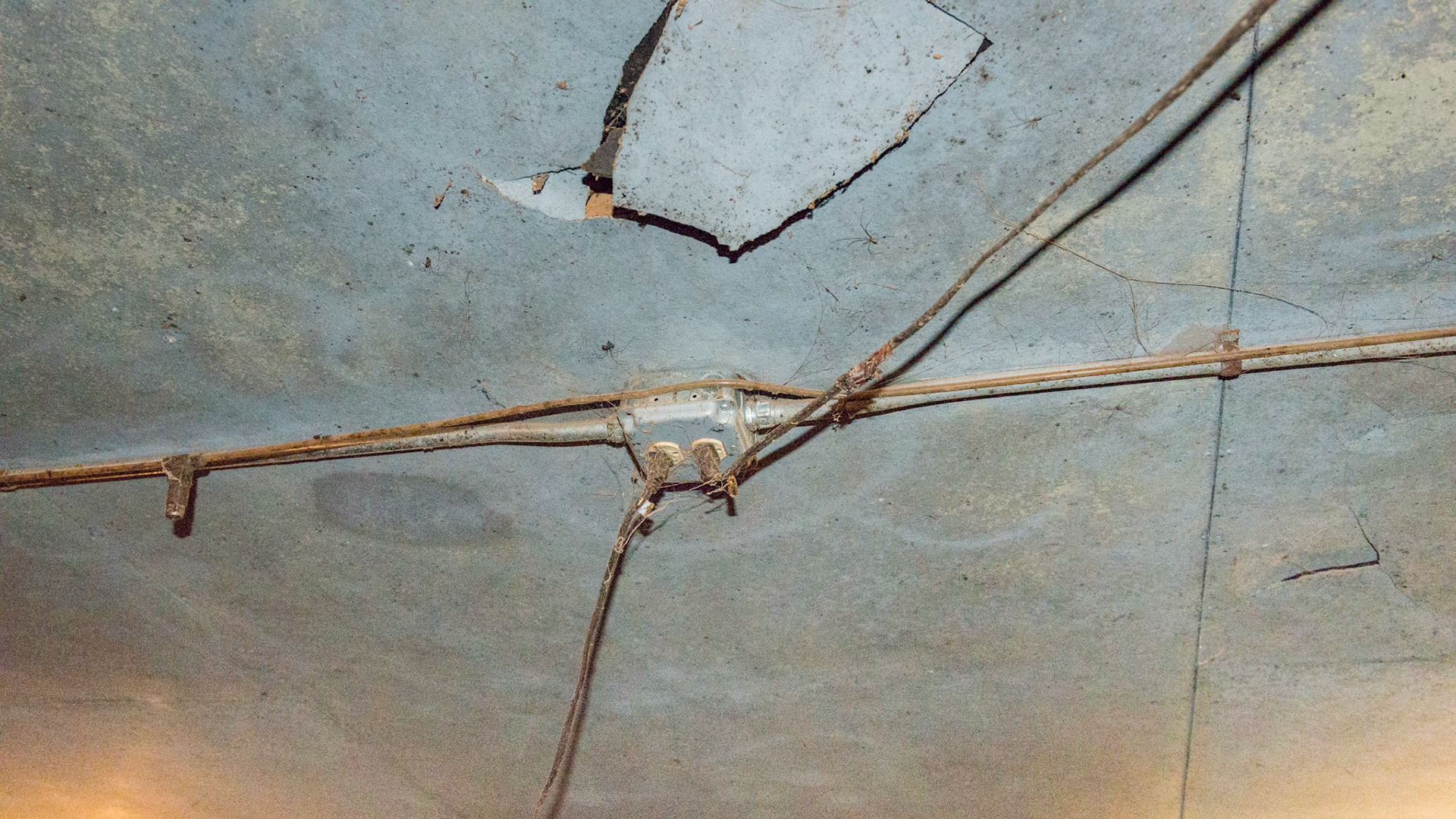 Loose and stretched electrical wire from a plug in the middle of the barn aisle going to the fans mounted in the stalls.  Cobwebs surround the outlet.