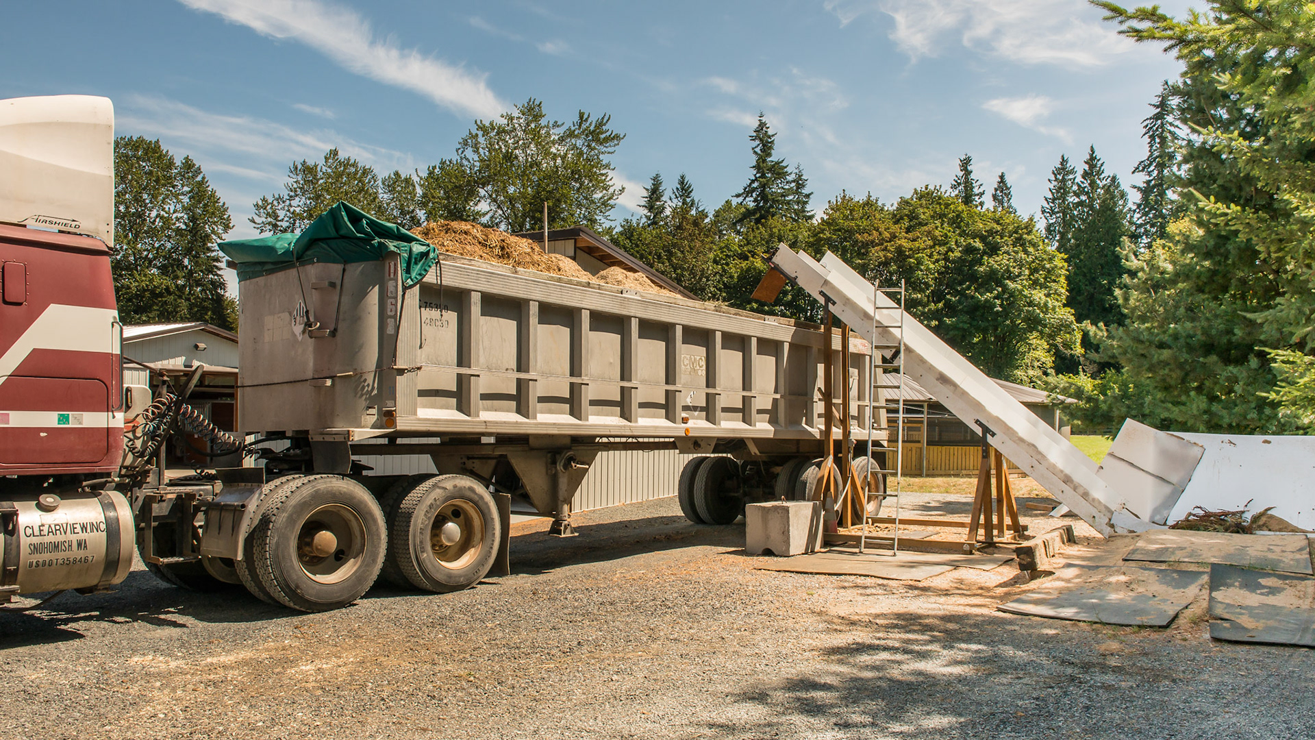 The manure spreader is backed up to the elevator and the manure is emptied into the hopper.  It then is carried up the elevator and emptied into the trailer.  The truck is moved forward to accommodate more waste then driven to the destination when full.