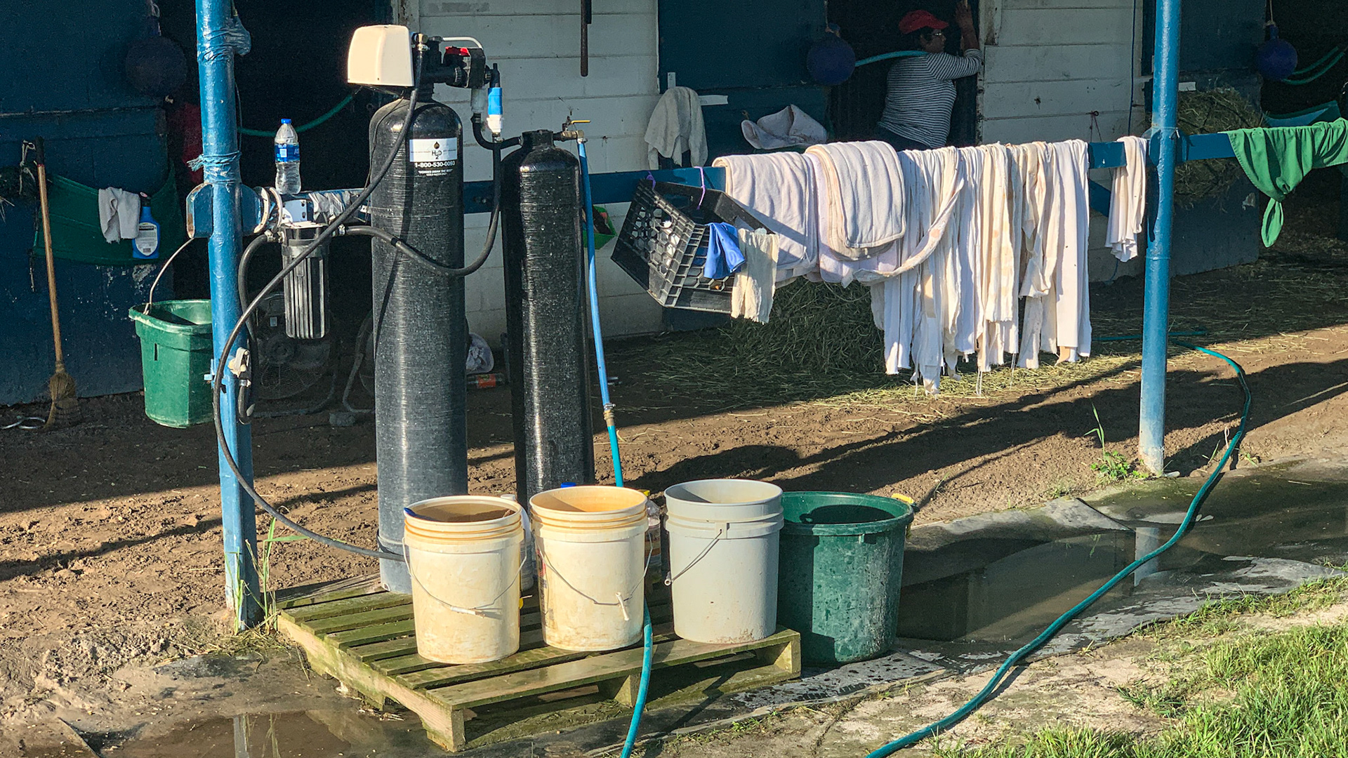 Carbon water filter system at a barn located in warm weather. The hose is being run from the spigot through the filters and into the stall in the background for the horse to drink.
