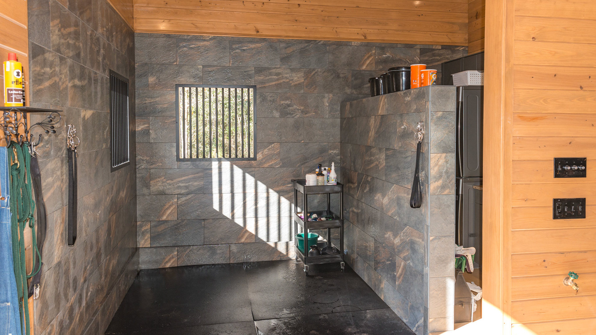 This wash rack is lined with porcelain tile adding beauty as well as functionality. On the other side of the partial wall is the washer and dryer, sink, and waterproof cabinets.  Everything can be hosed down.