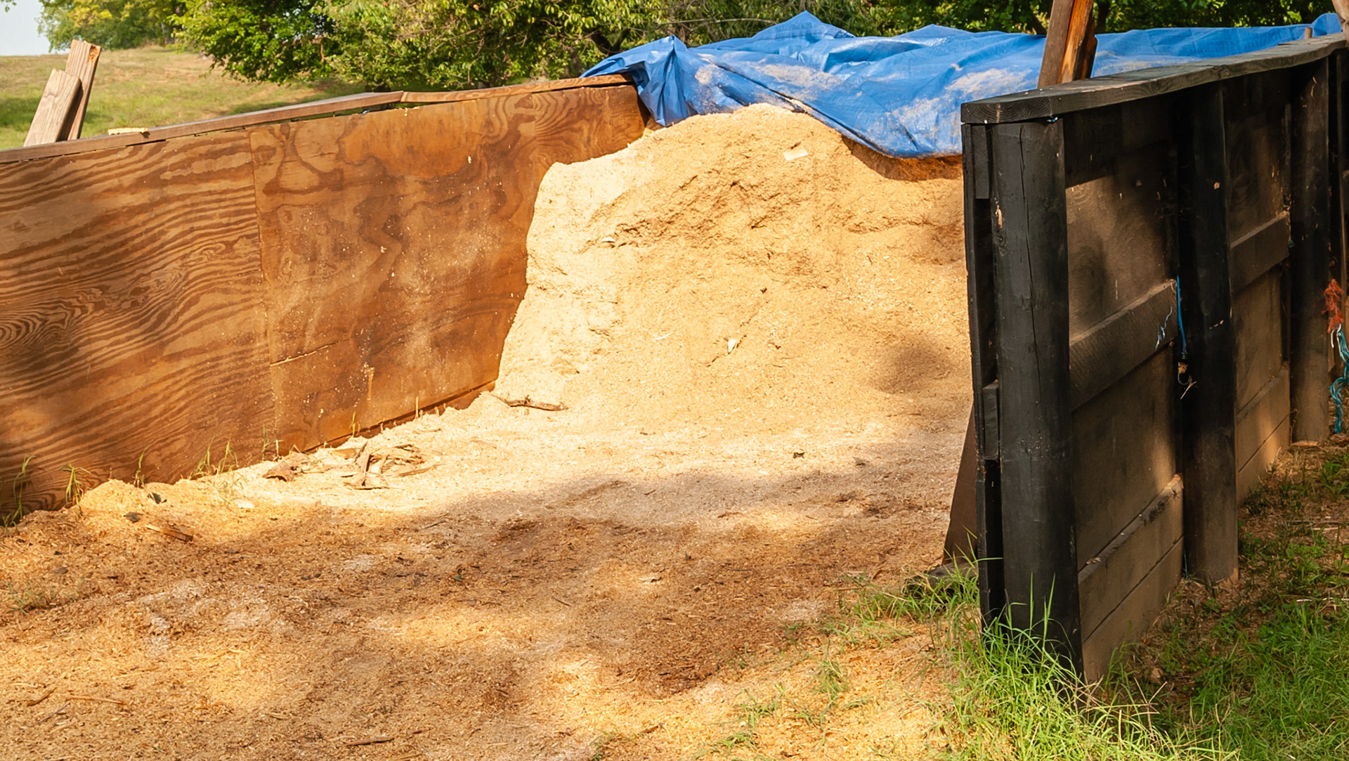 Shavings kept outdoors in a containment area and covered with a tarp.