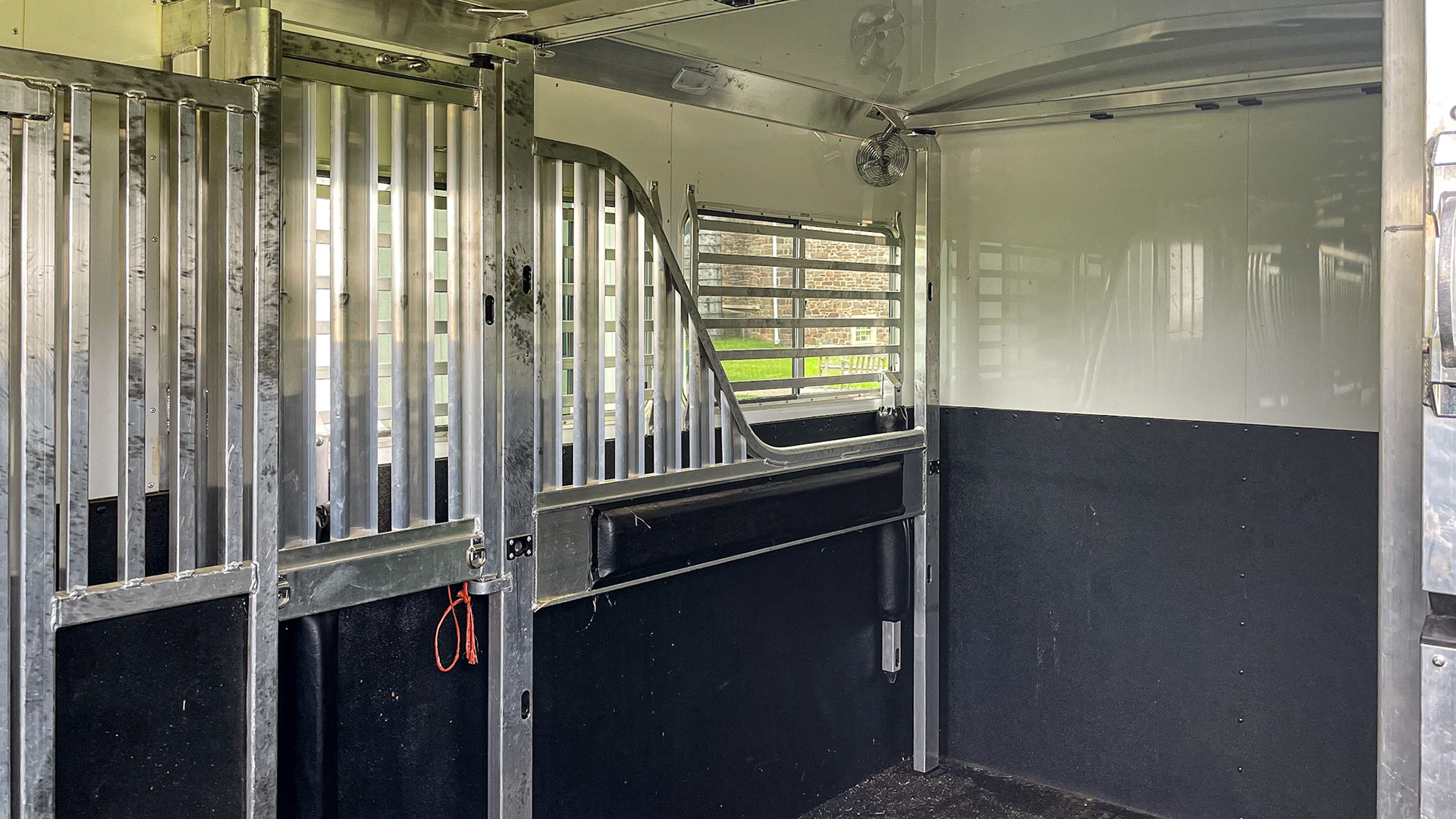 A gooseneck trailer on a pickup truck. The lightweight but strong aluminum stall partitions can slide into any position creating various stall widths. The windows have protective bars. There is a ceiling fan mounted in the corner.