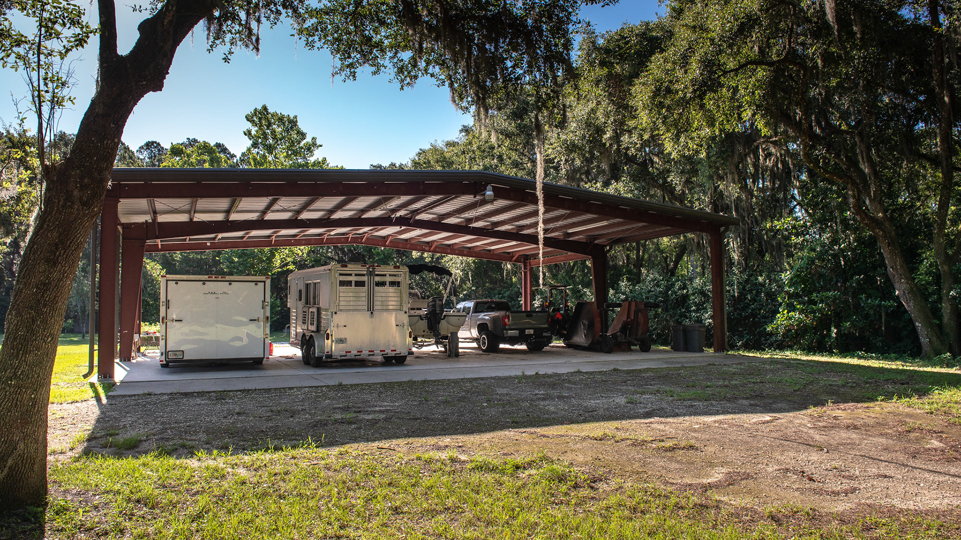 Trailer, car, and equipment under a steel roof and on a concrete pad.