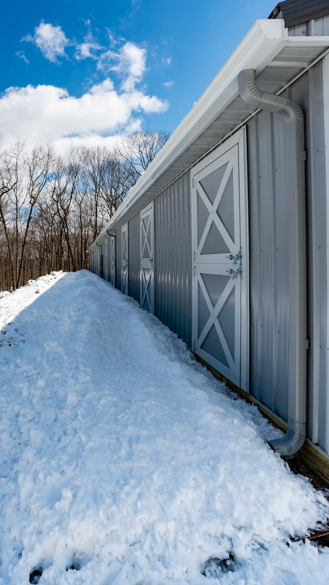 Snow falling off of roof prevents opening of emergency back doors to stalls. - Eve troughs direct roof runoff away from edge of the barn and into downspouts to prevent mud outside of the stall doors.