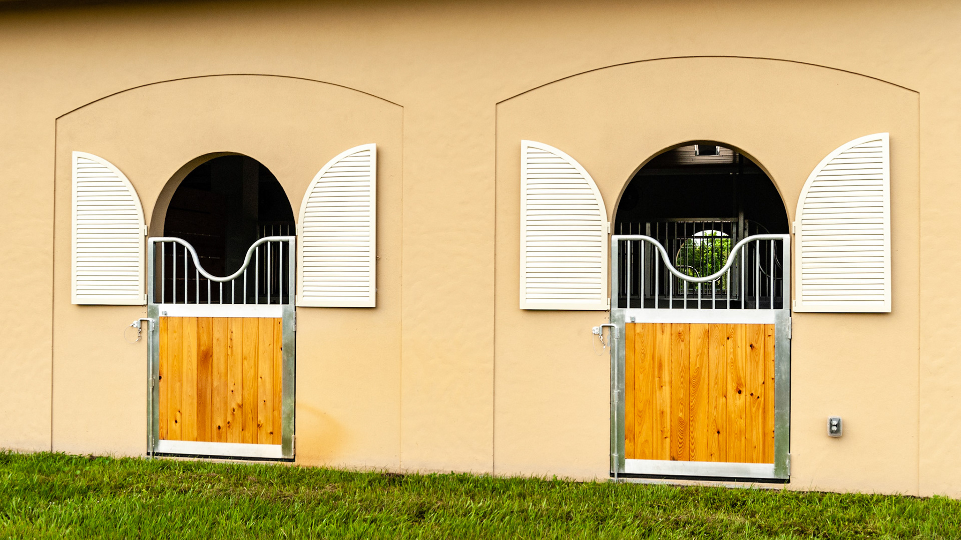 Custom outside stall door with one latch coupling the upper and lower parts of the door at the same time. Upper slatted metal doors can close the top against driving rain or sun.