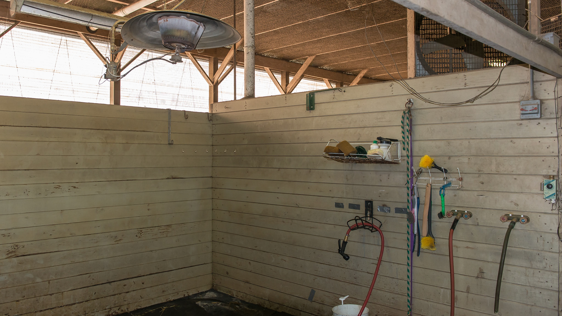 A gas powered heater over a wash stall in a barn has a live pilot flame.