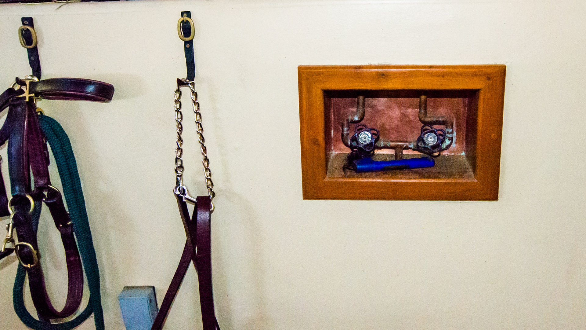 Copper pipe water controls outside of a stall, forged tack hooks in the shape of leather buckels.