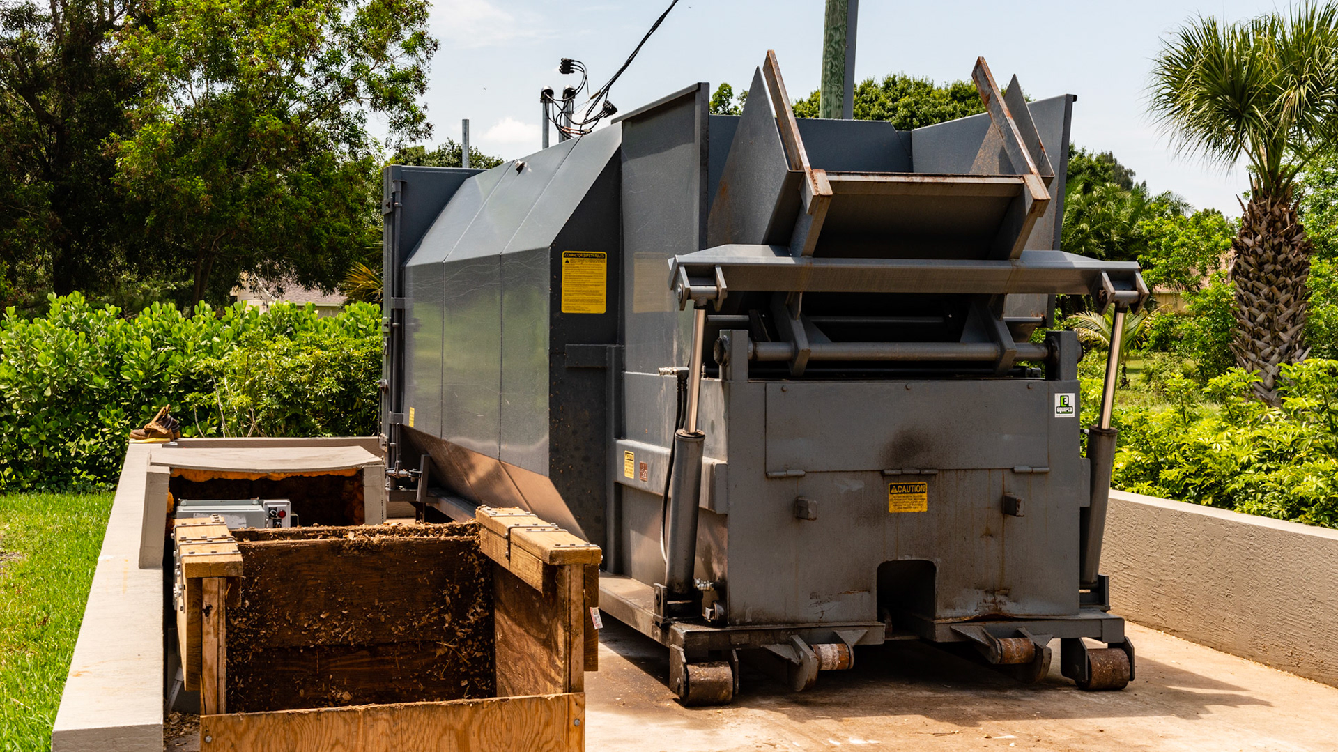 A trash compactor is used for manure disposal on this 100 horse farm. Note the cement container area to prevent environmental spillage.  The manure is loaded into the wooden container which is lifted and dumped, then compressed.  The whole unit is exchanged by a roll-back truck.
